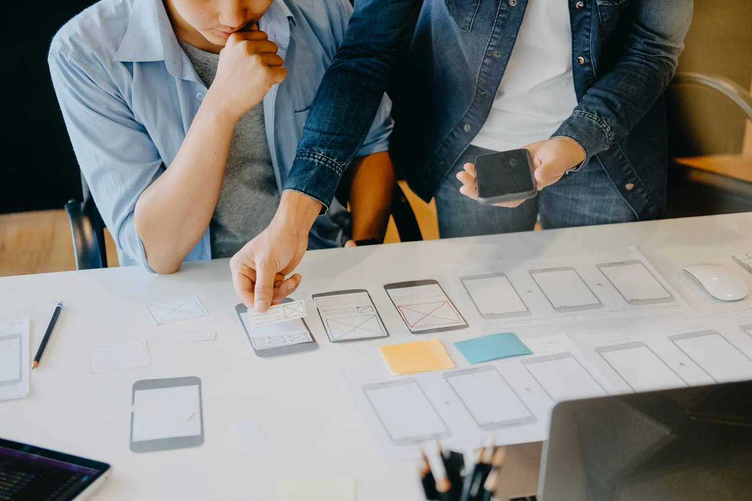 Two people at a desk testing layouts on paper mockups of cell phones