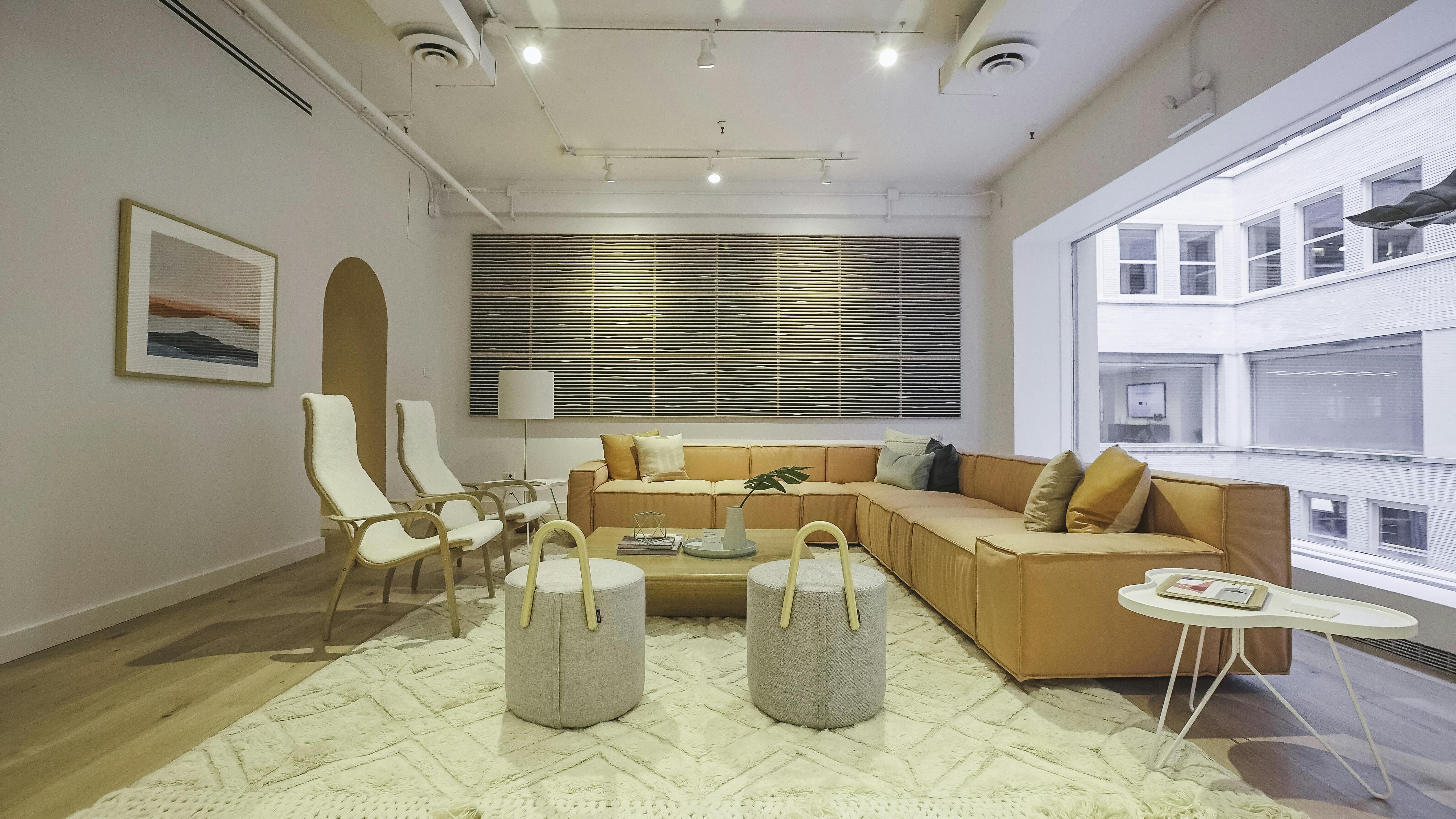 Image of Hightower's showroom with a pale peach colored sectional, two Lamino chairs with white sheepskin, and two Amstelle Poufs. The room has a white rug and wood floors.