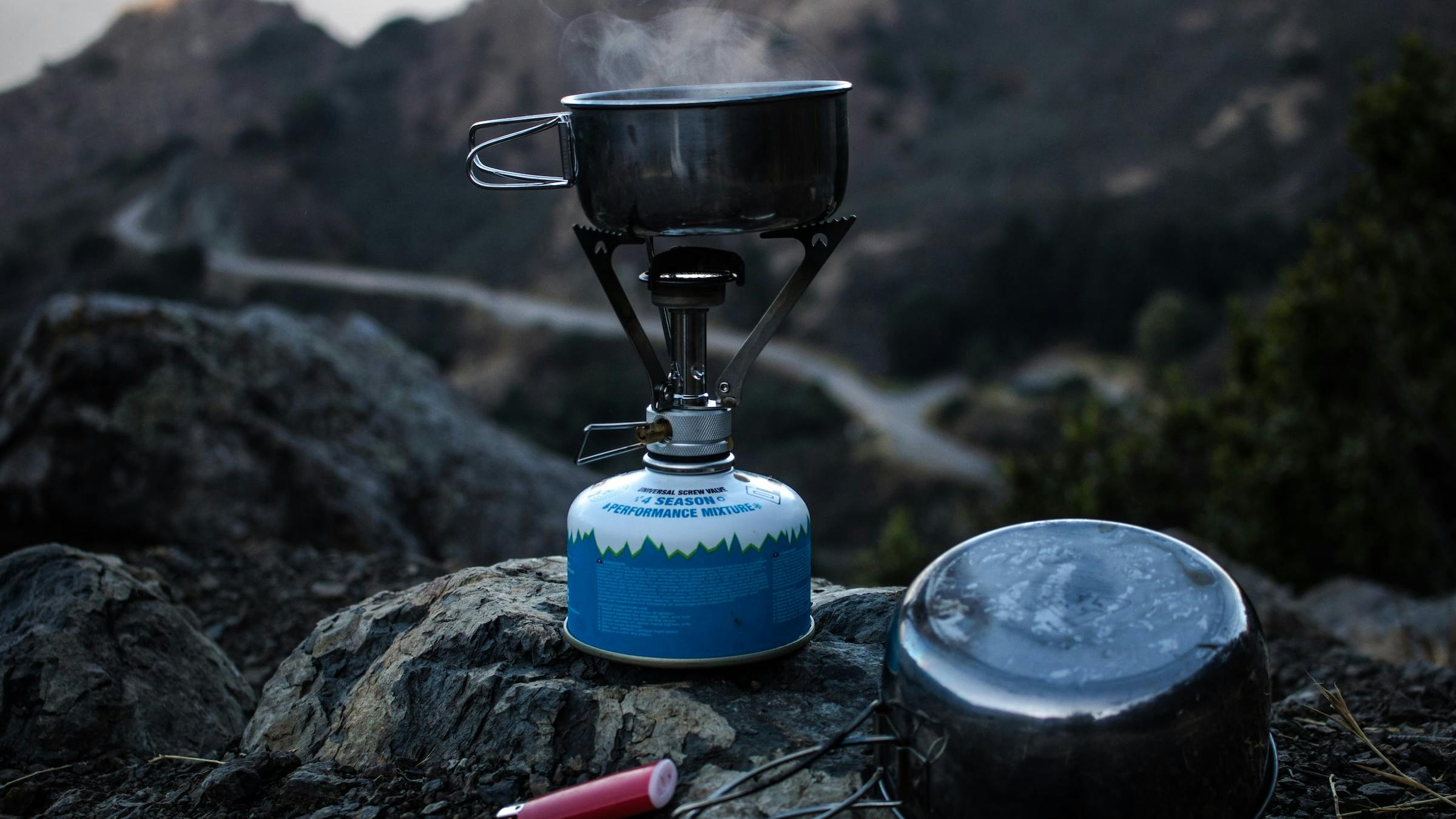 A canister stove being used to boil water in mountainous terrain.