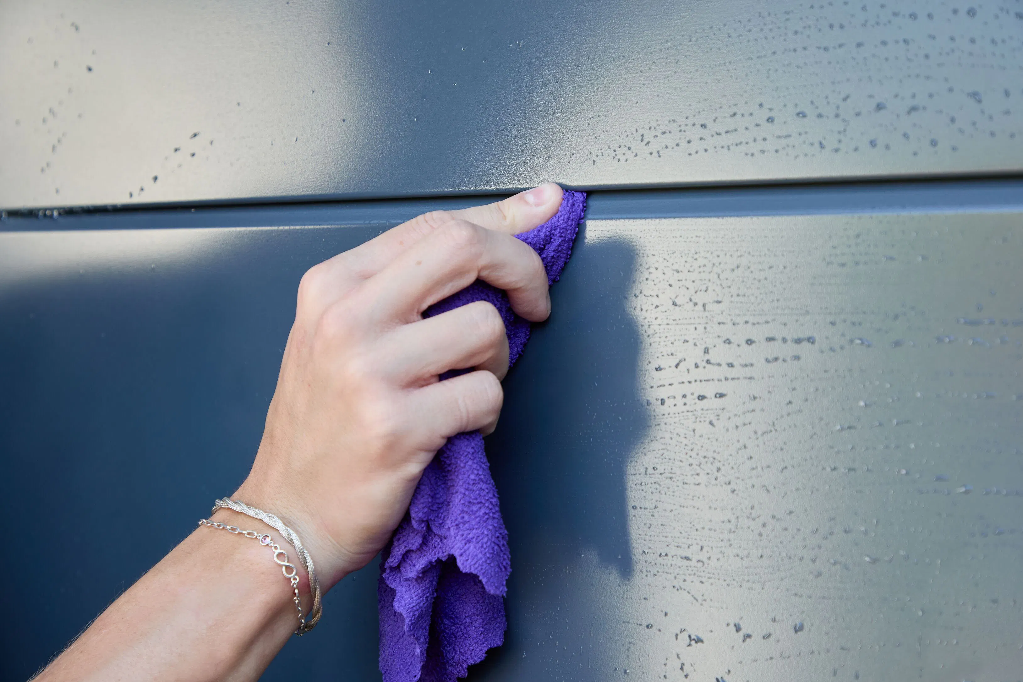 Person cleaning an anthracite grey garage door with a purple cloth, wiping between panel joins on the damp surface.