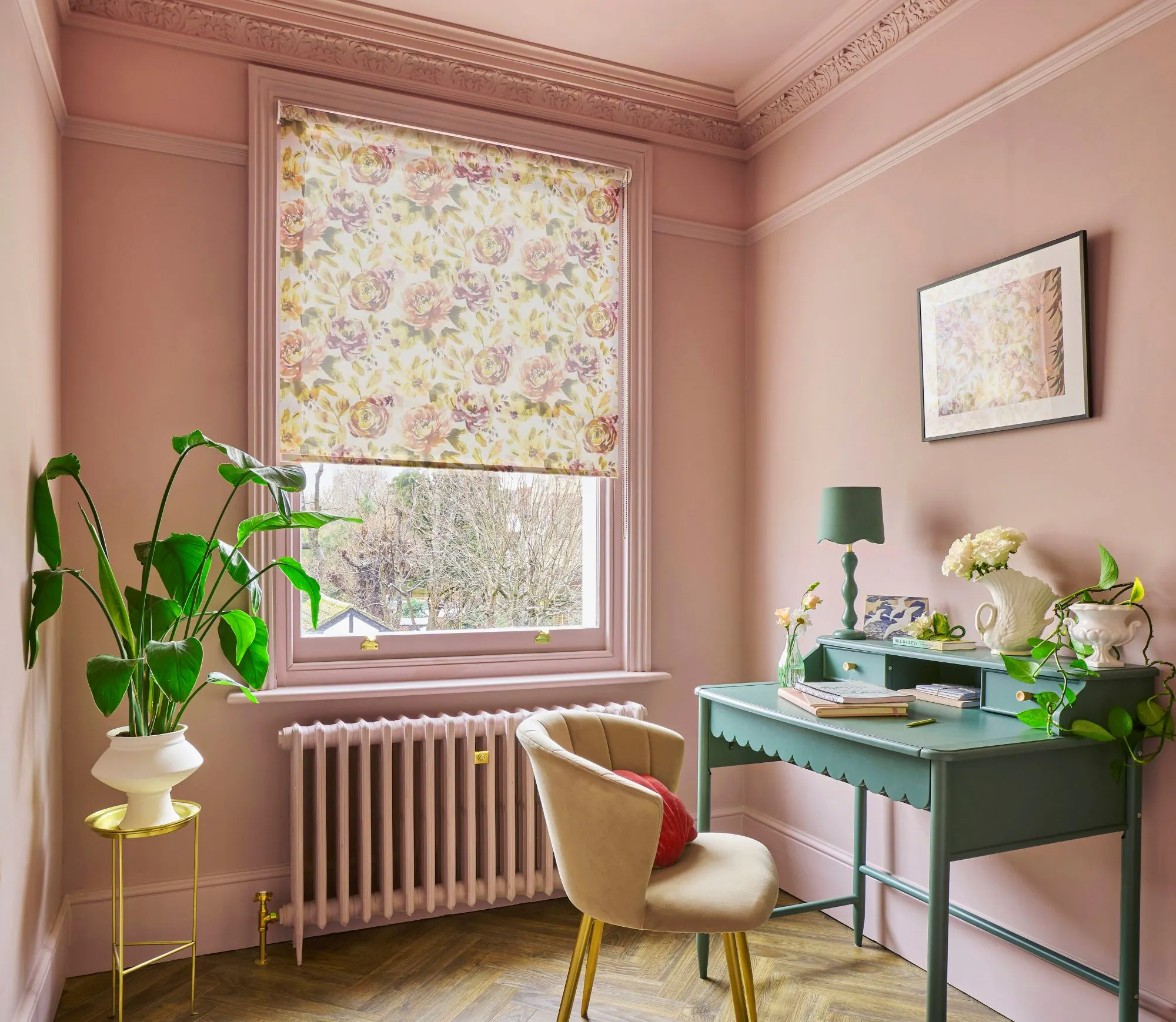 Watercolour floral roller blind in a blush pink home office, paired with a green desk, indoor plants and decorative mouldings.