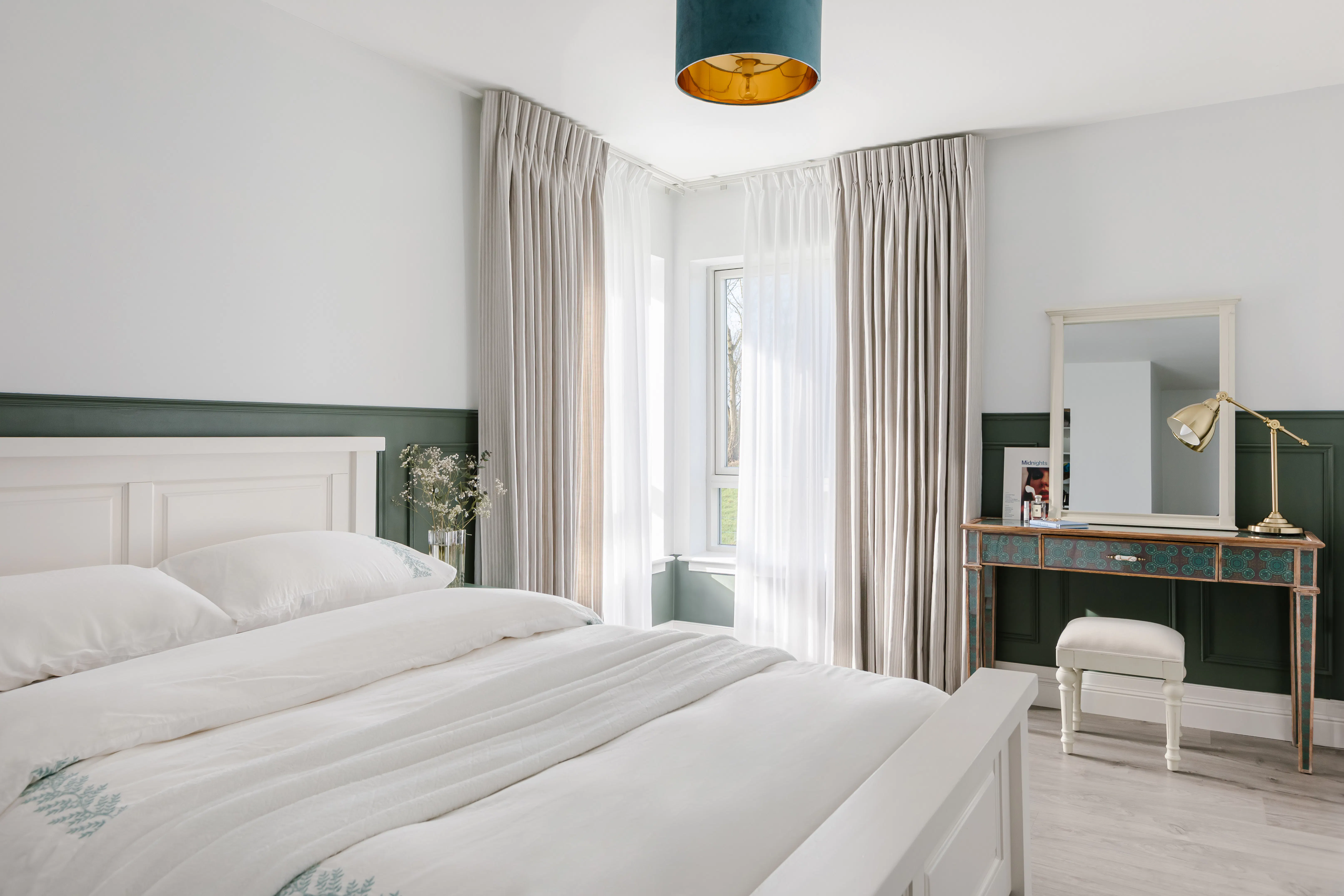 Airy bedroom with tall windows dressed in sheer curtains and soft drapes, allowing daylight to brighten the white bed and calm décor.