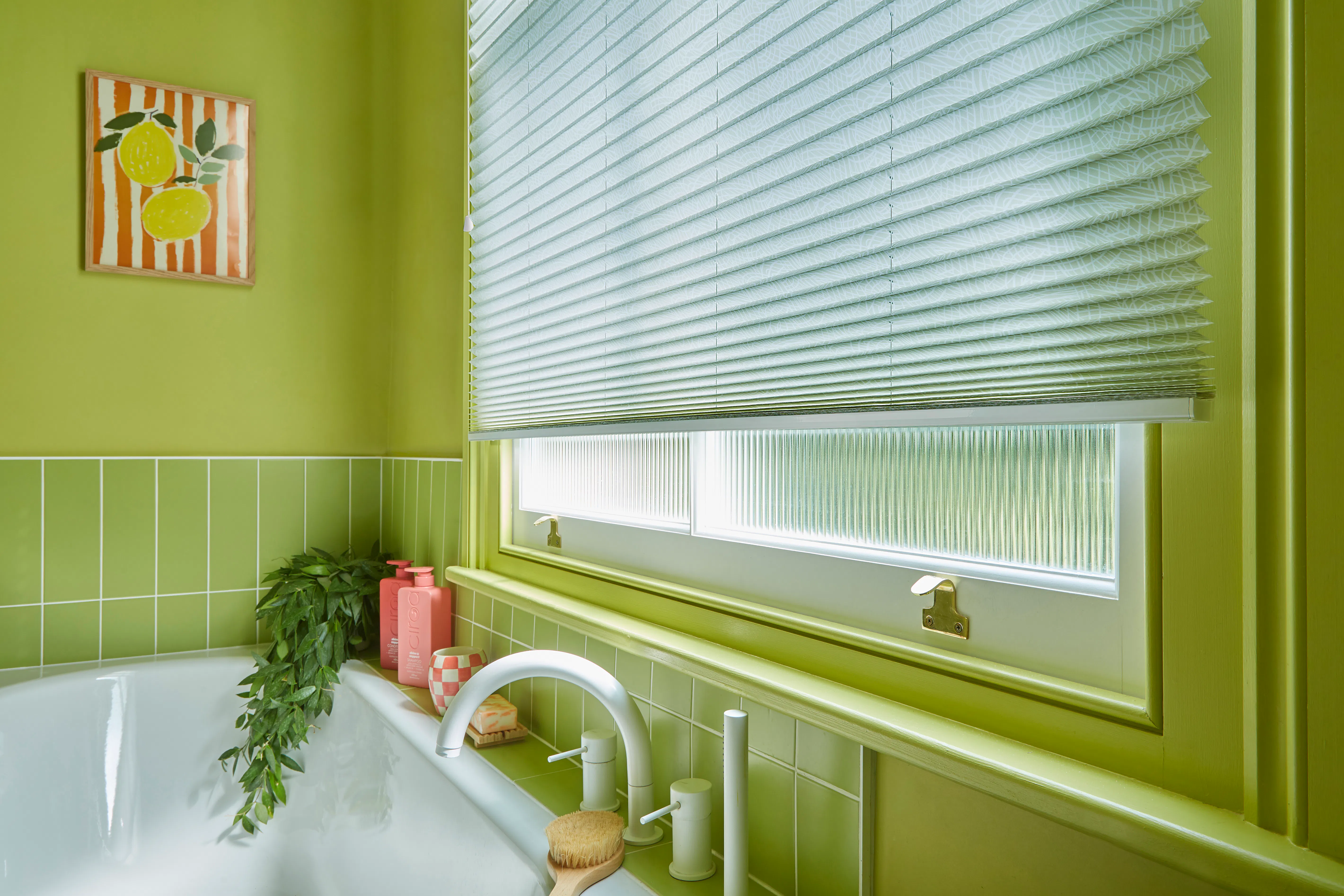 Pleated blind fitted to a bathroom window, complementing vibrant green walls and tiling beside a white bath.