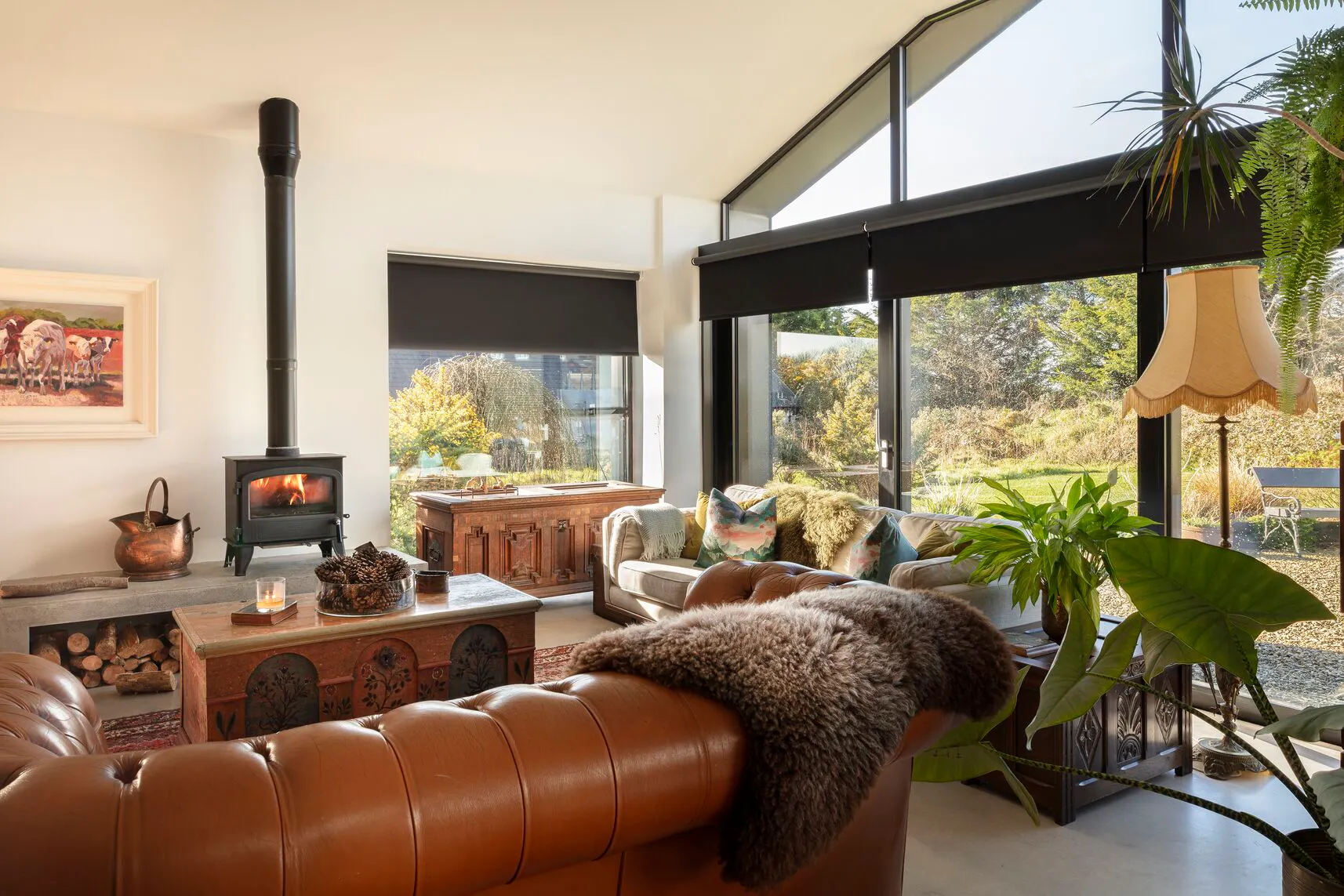 Spacious living room with floor-to-ceiling windows and black-framed glazing, fitted with Roller blinds overlooking a leafy garden and flooding the space with light.