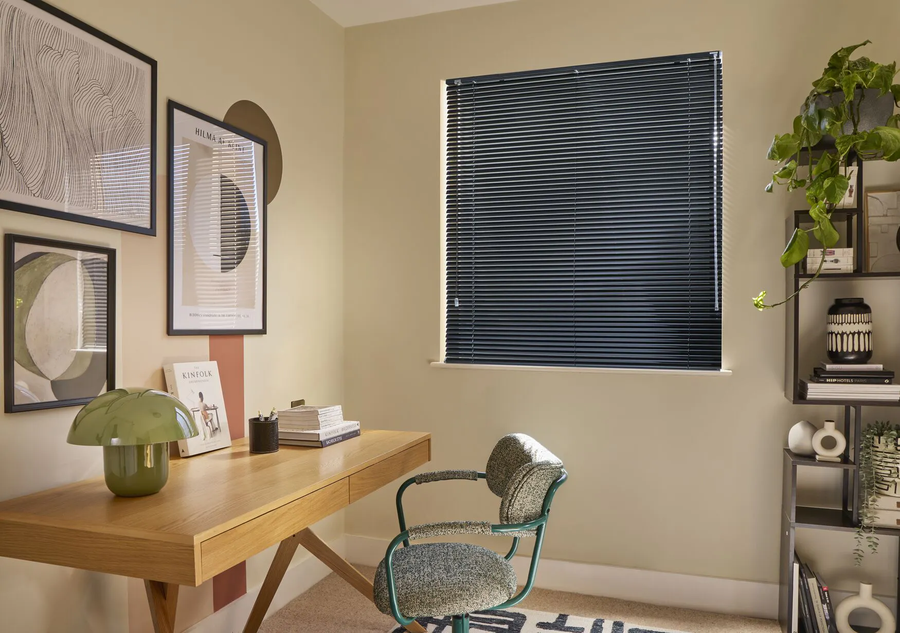 Black gloss metal Venetian blind in a modern home office with wooden desk, shelving and framed wall art.