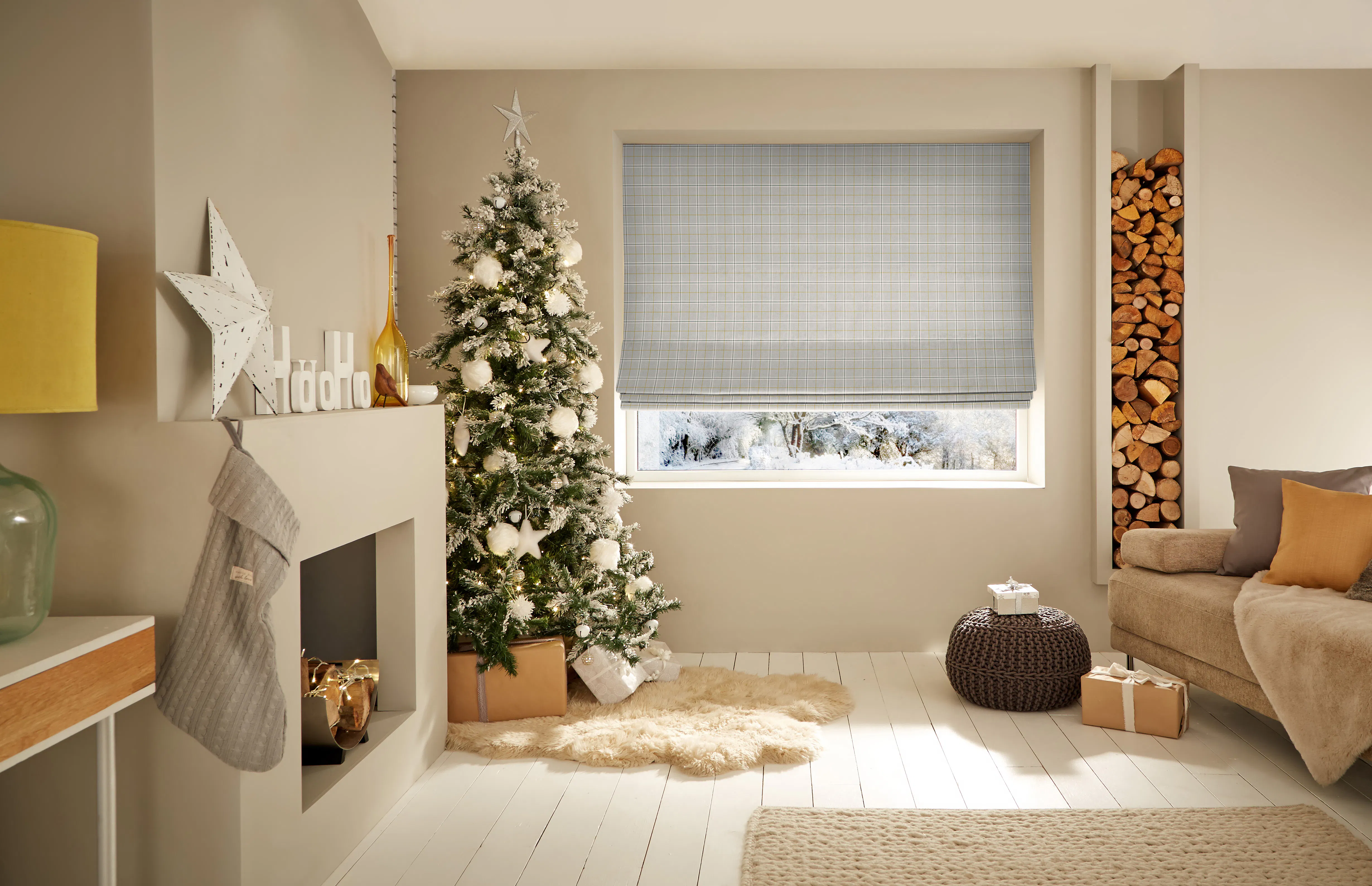 Bright living room with a wide window fitted with a checked Roman blind, beside a snow-dusted Christmas tree and fireplace.