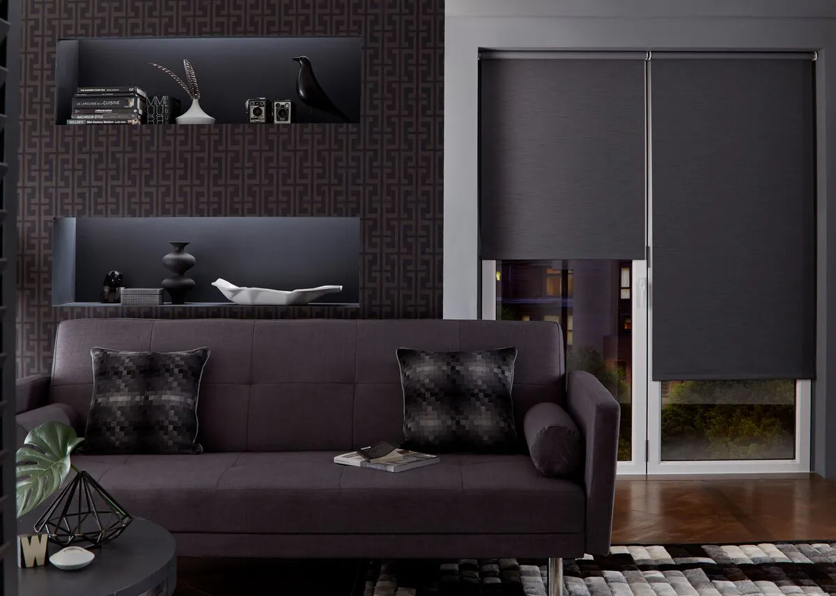A moody modern living room with a dark sofa, a polished dark-wood floor and charcoal Roller blinds fitted to patio doors.
