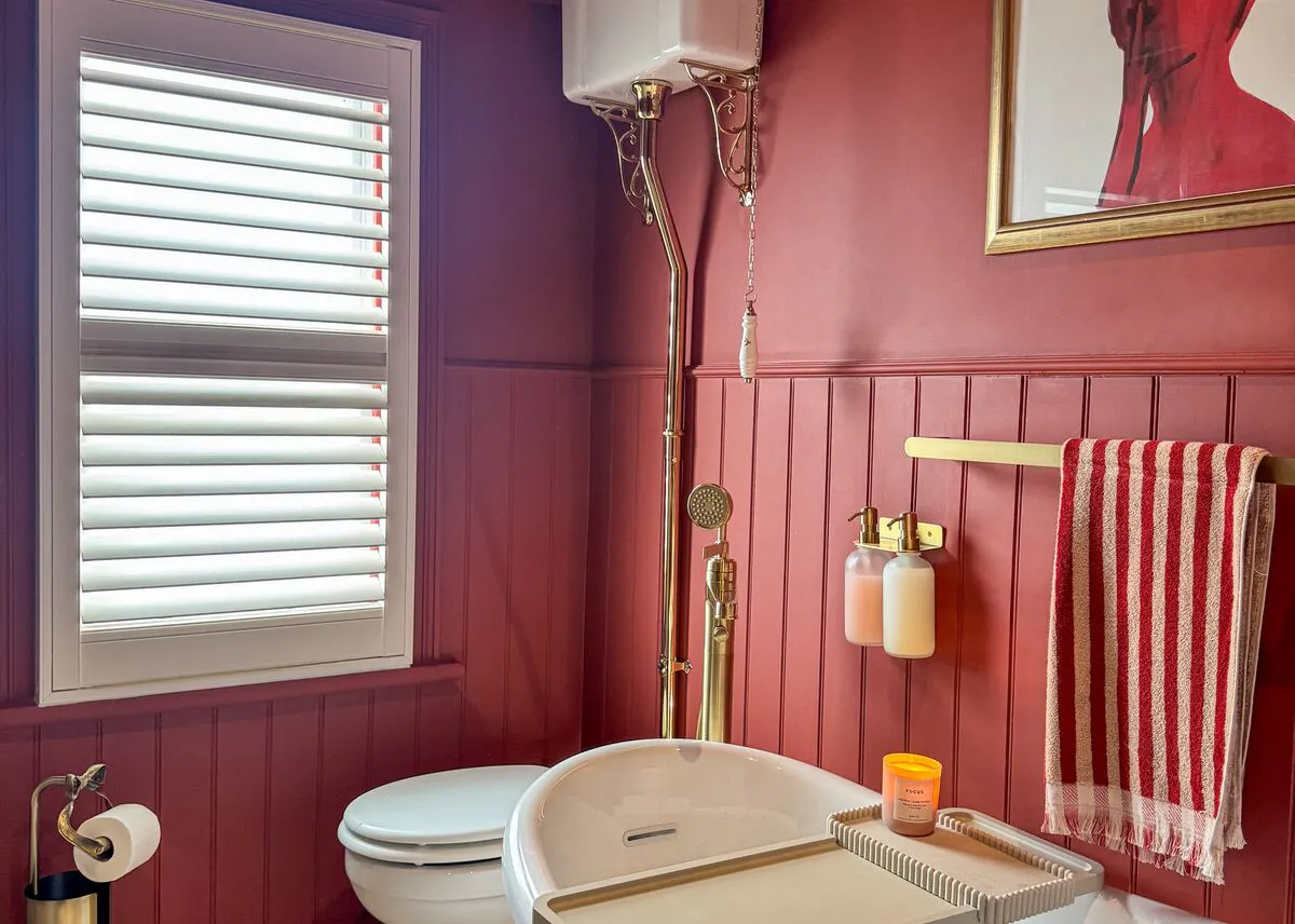 White shutter fitted to a bathroom window, bringing privacy and light control to a bold red scheme with a freestanding bath.