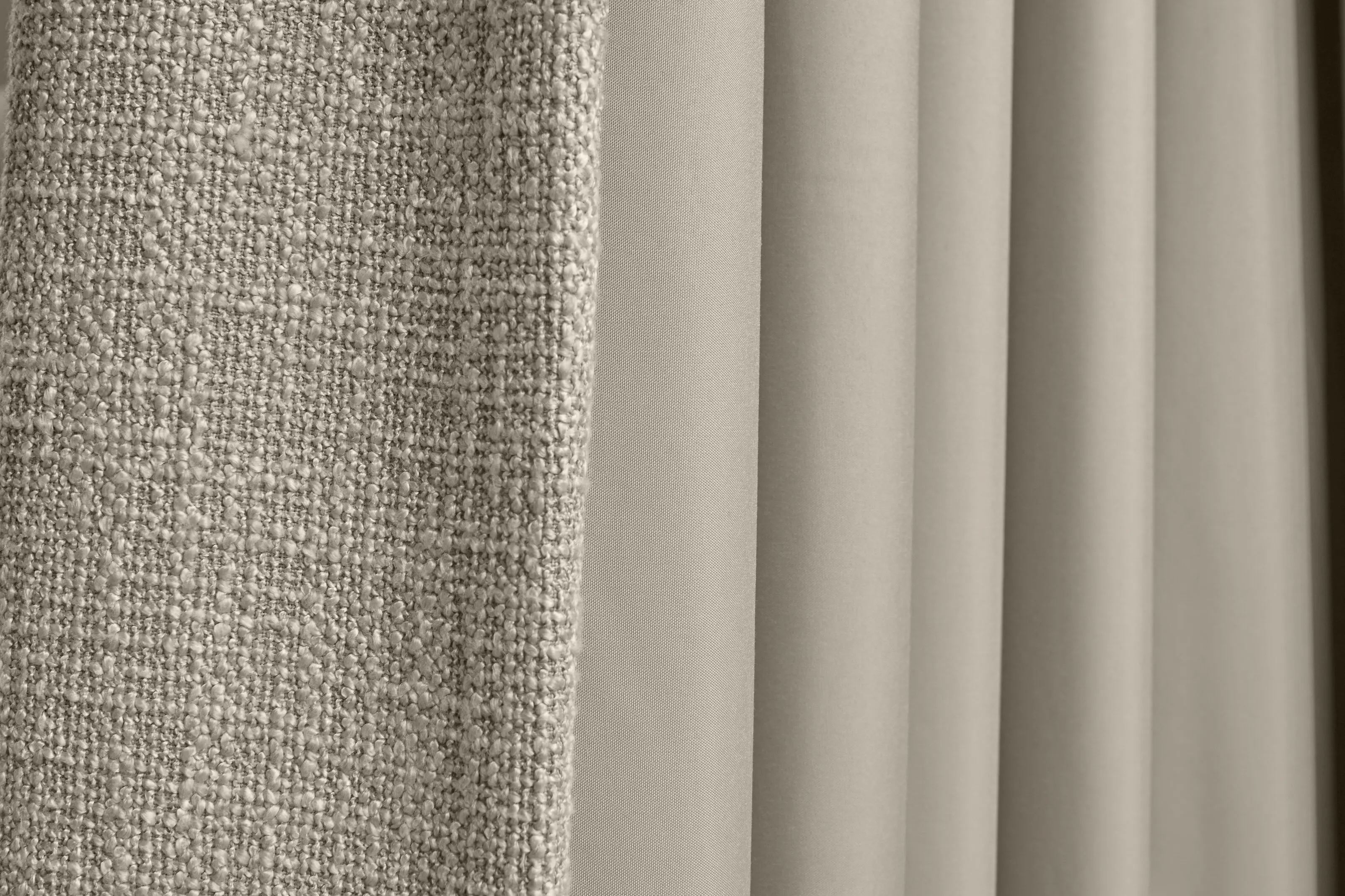 Close-up of neutral beige curtains, showing contrasting textures with a chunky woven fabric beside soft, smooth pleated drapes.