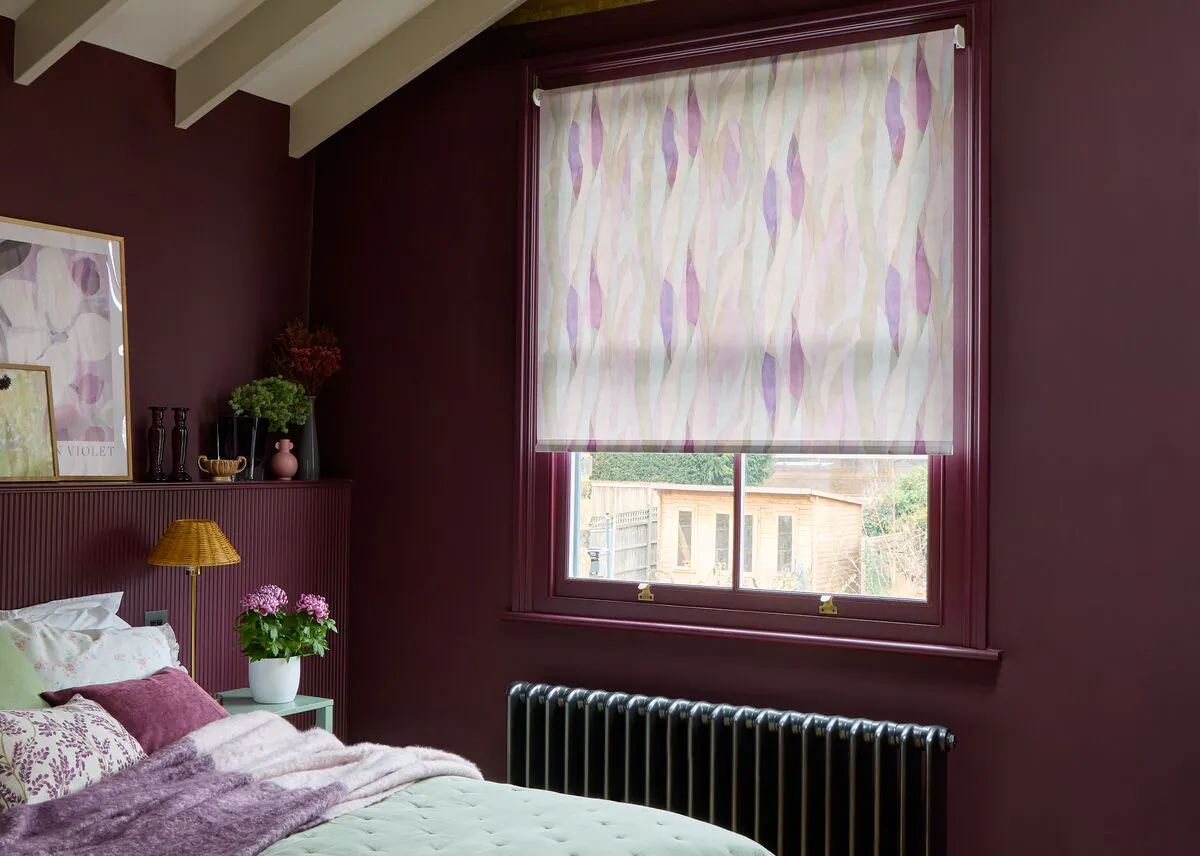 Calix Amethyst patterned roller blind in a plum-coloured bedroom with soft purple tones and coordinated floral décor.