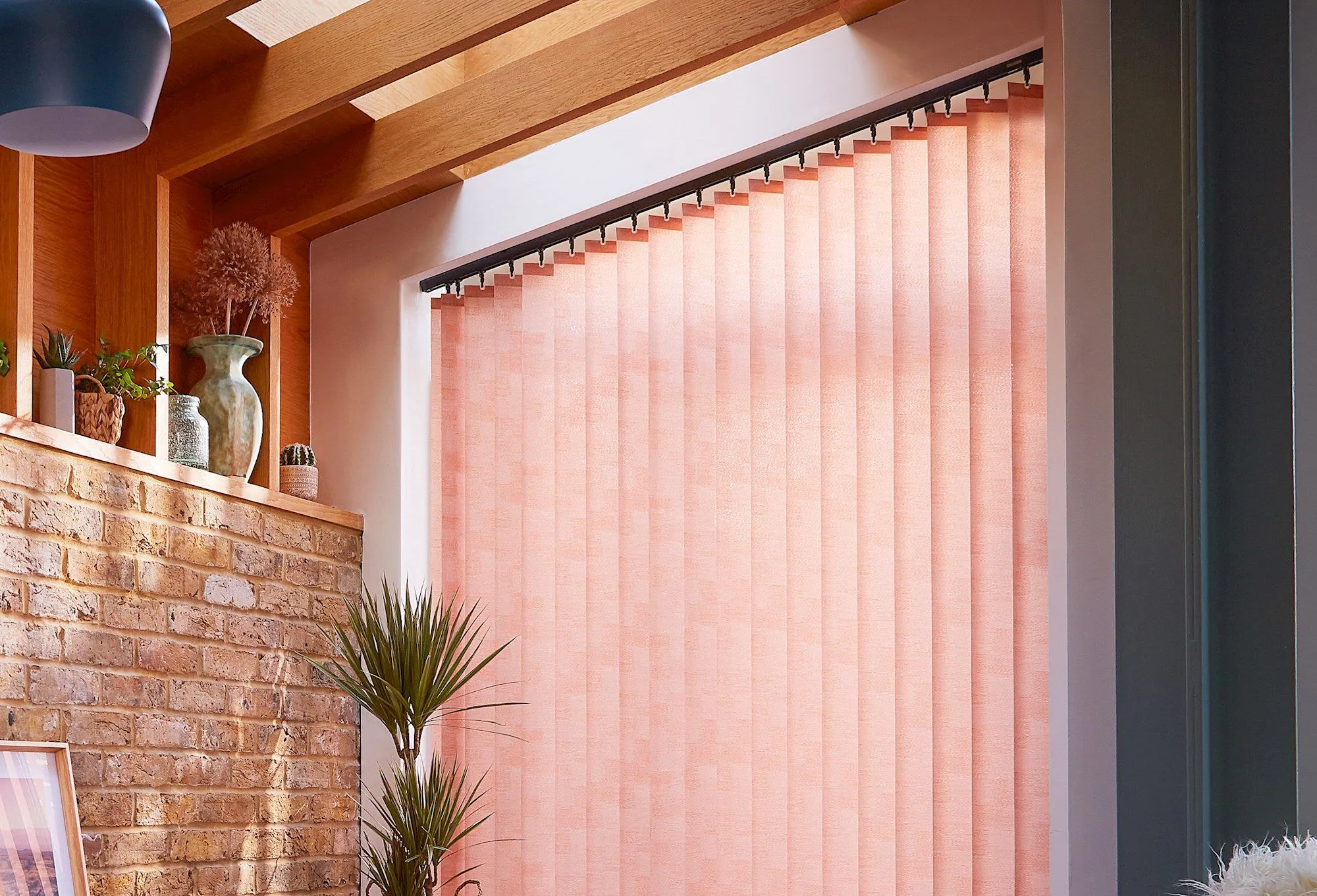 peach coloured vertical blinds fitted on a wide window in a living room with exposed brick work and wood slats