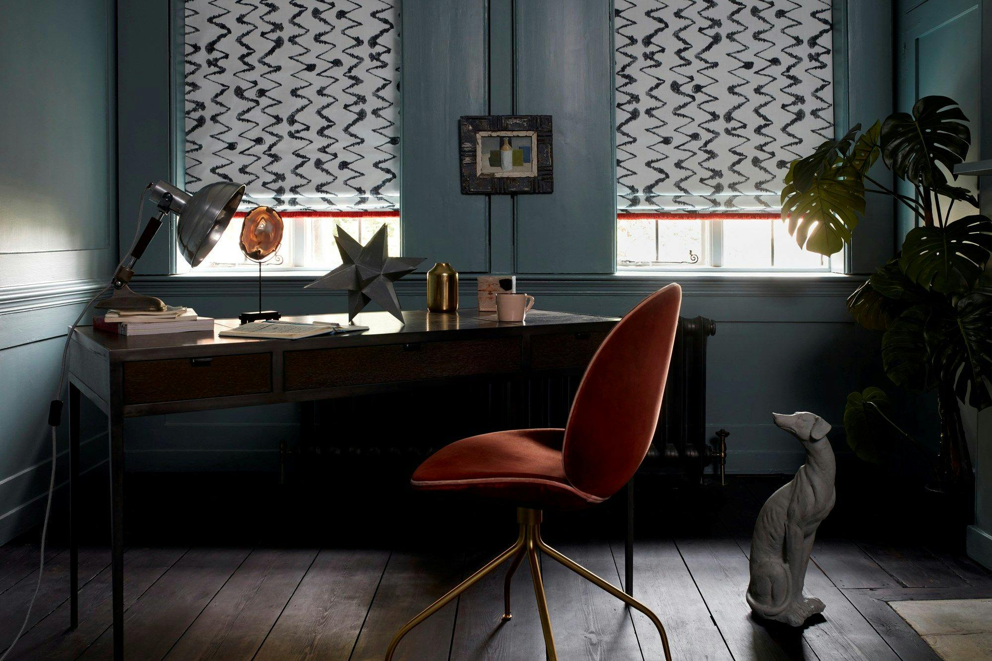 Black and white styled Abigail Ahern roman blinds with a zig zag pattern fitted to rectangular windows in a study with blue walls