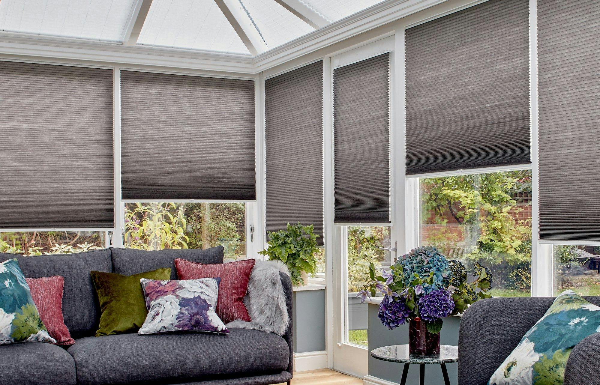 dark grey pleated blinds at different heights on conservatory windows behind grey sofas