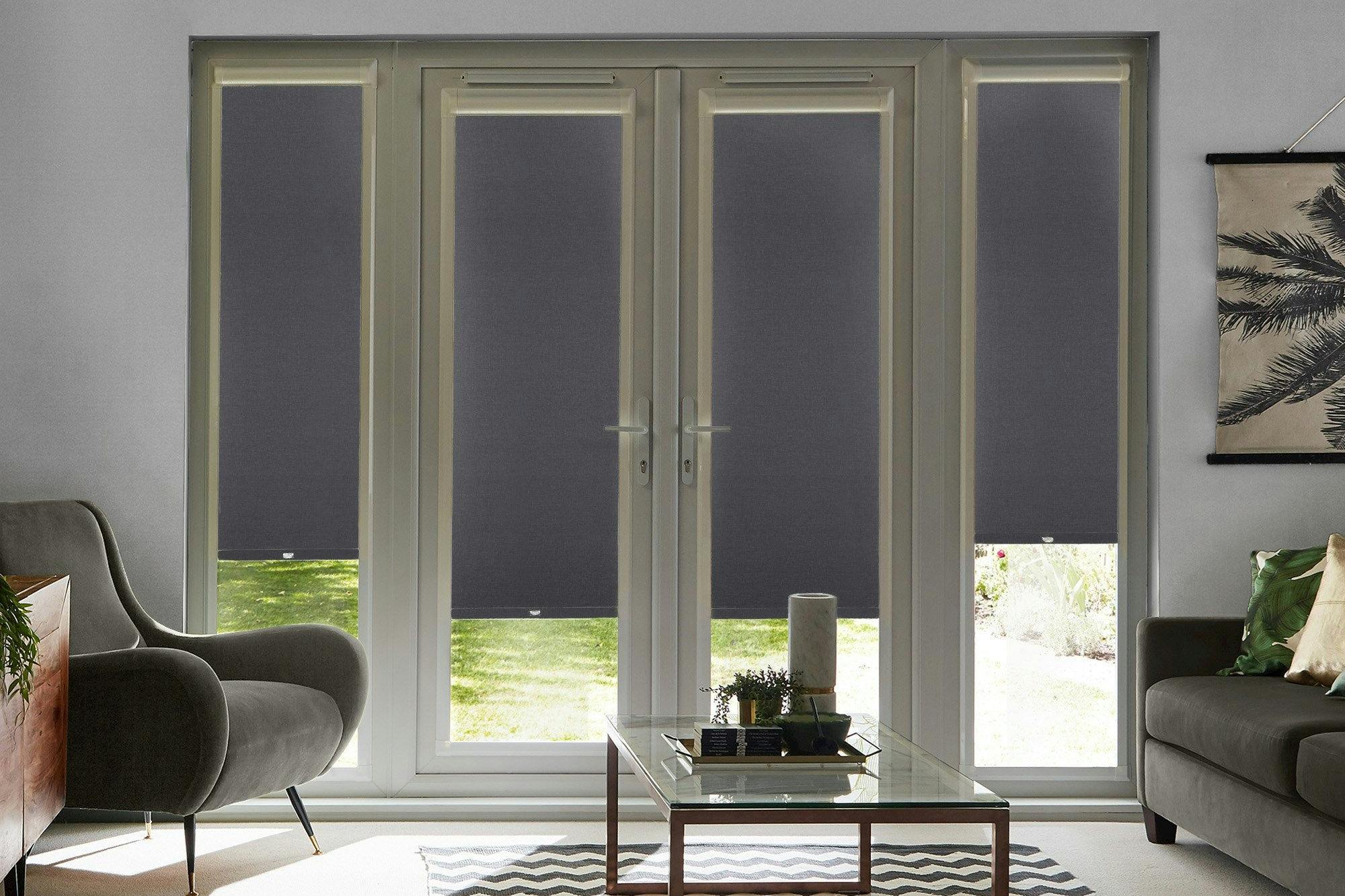 Acacia Black Perfect Fit Roller blinds on four French Doors in a modern living room. The blinds are black and contrast against a sofa, armchair and coffee table.