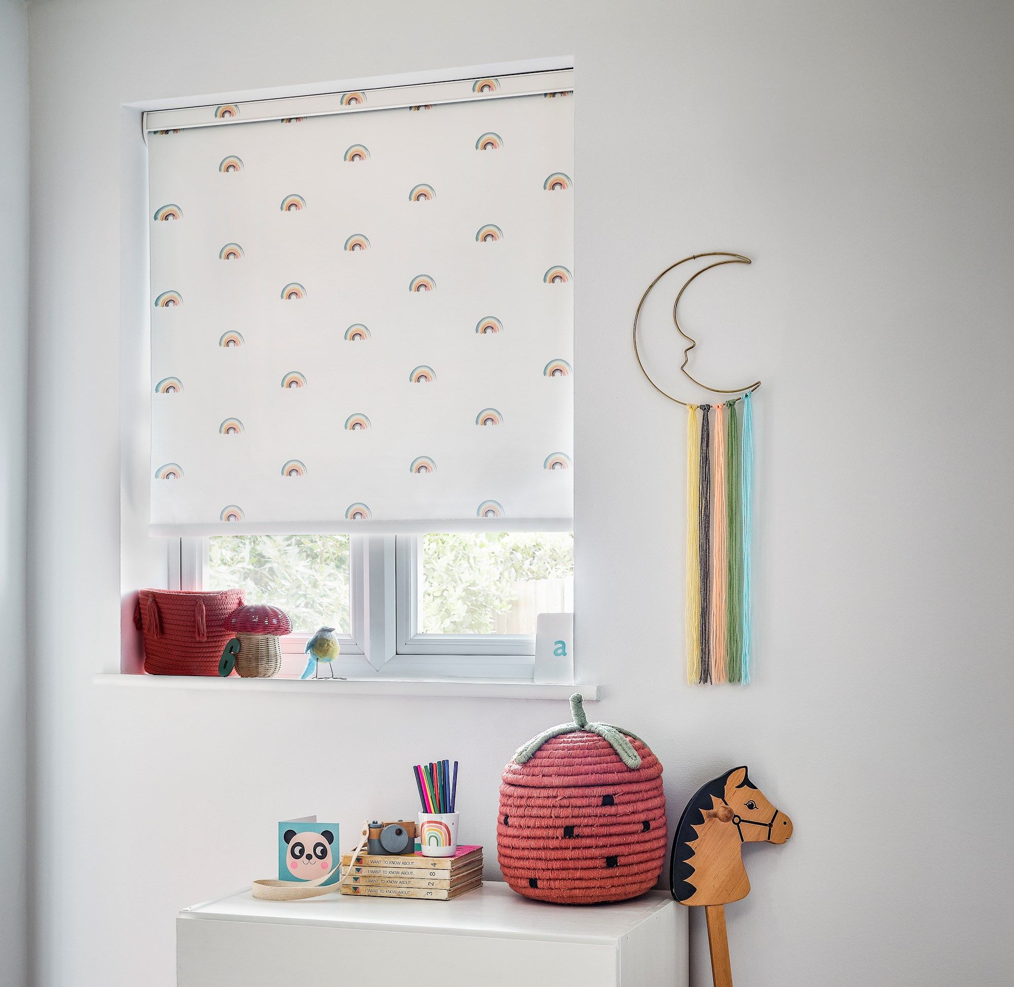 white roller blind with mini rainbows on in a childs bedroom window with childrens decoration and a hobby horse