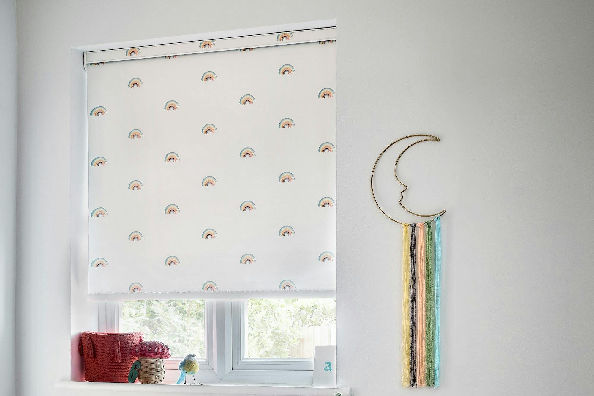 white roller blind with mini rainbows on in a childs bedroom window with childrens decoration and a hobby horse