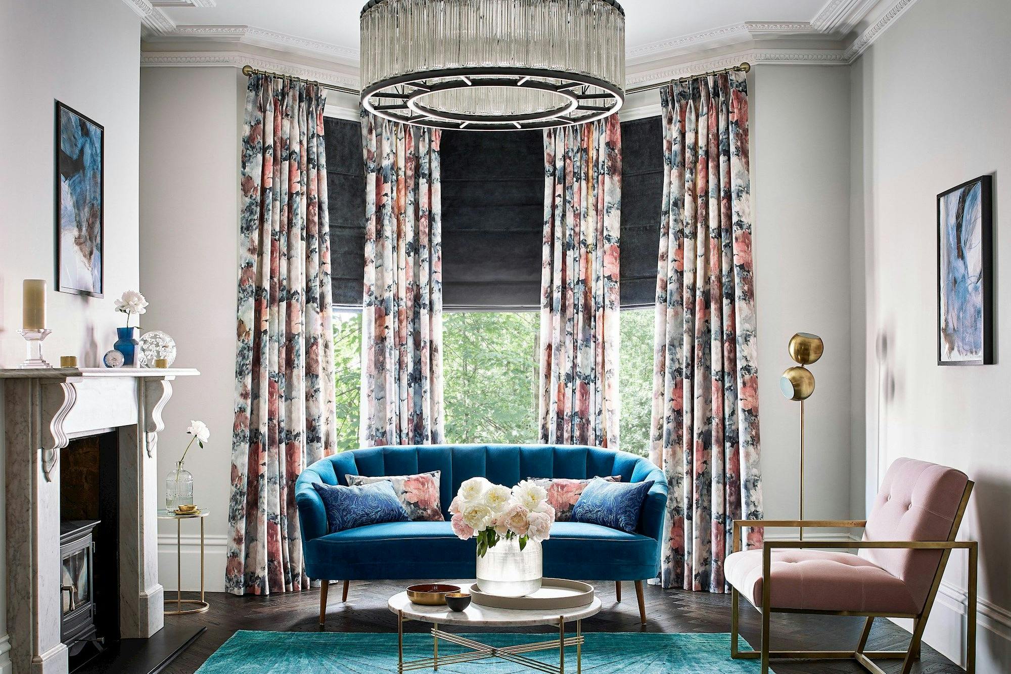 Dark grey velvet roman blind under floral print curtains in a bright living room with blue and rose pink accents
