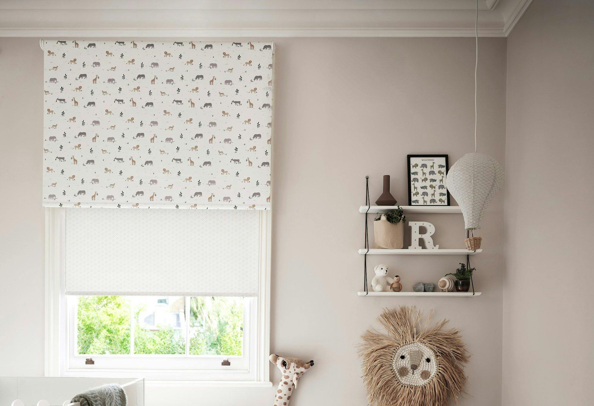 Blinds with animal patterns cover a window in a nursery. Nearby, shelves hold toys, a framed "WILD THING" print, and a decorative "R". A woven lion face decorates the wall.