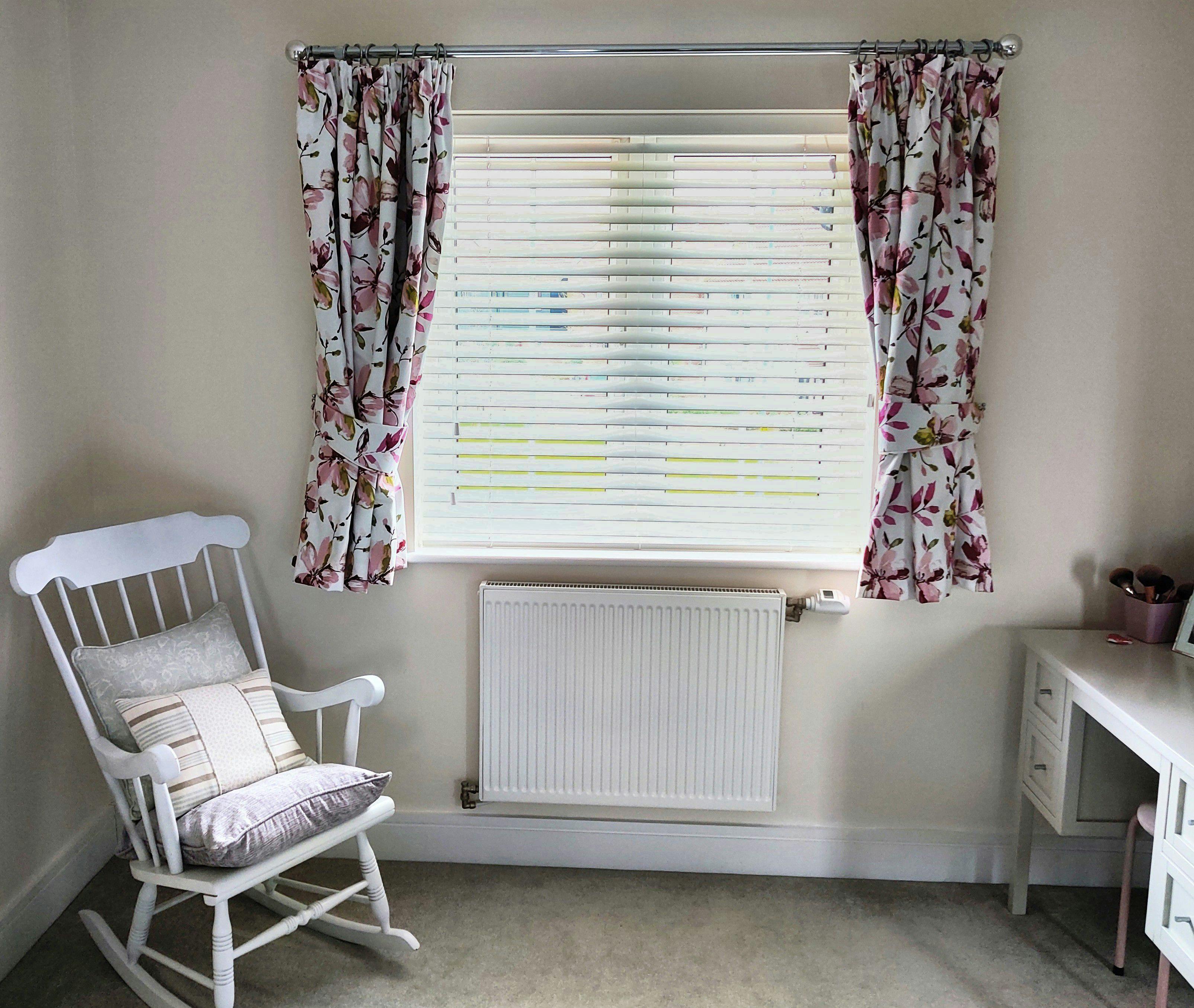White curtains with a colourful floral print over venetian blinds in a neutral room