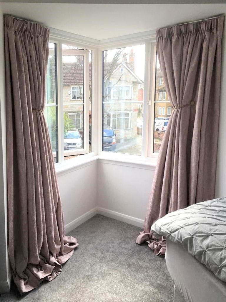 Blush pink pinch pleat curtains in a corner window 