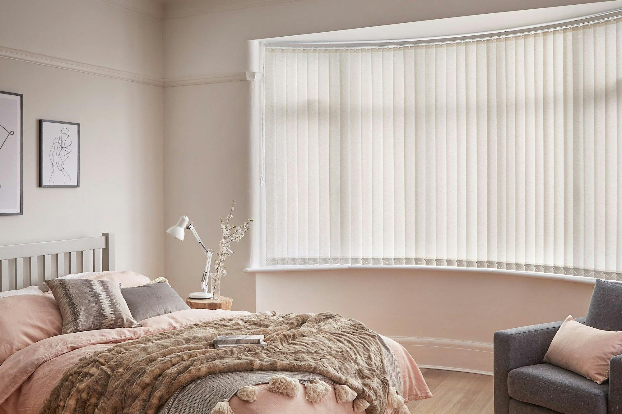Minimal luxe bedroom with soft furnishings and a bow window dressed with light cream vertical blinds