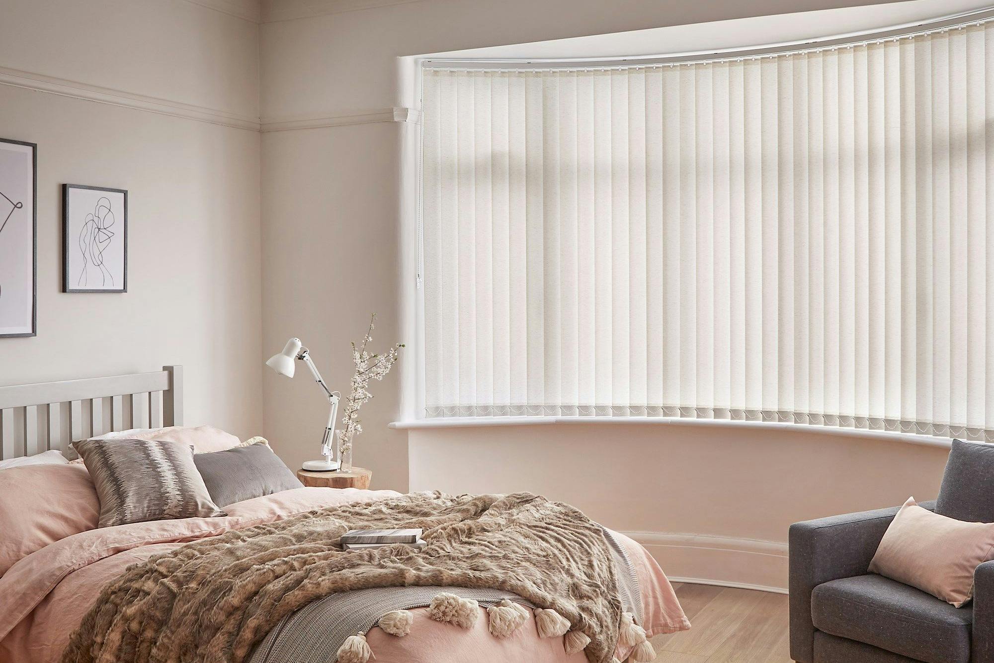 Minimal luxe bedroom with soft furnishings and a bow window dressed with light cream vertical blinds