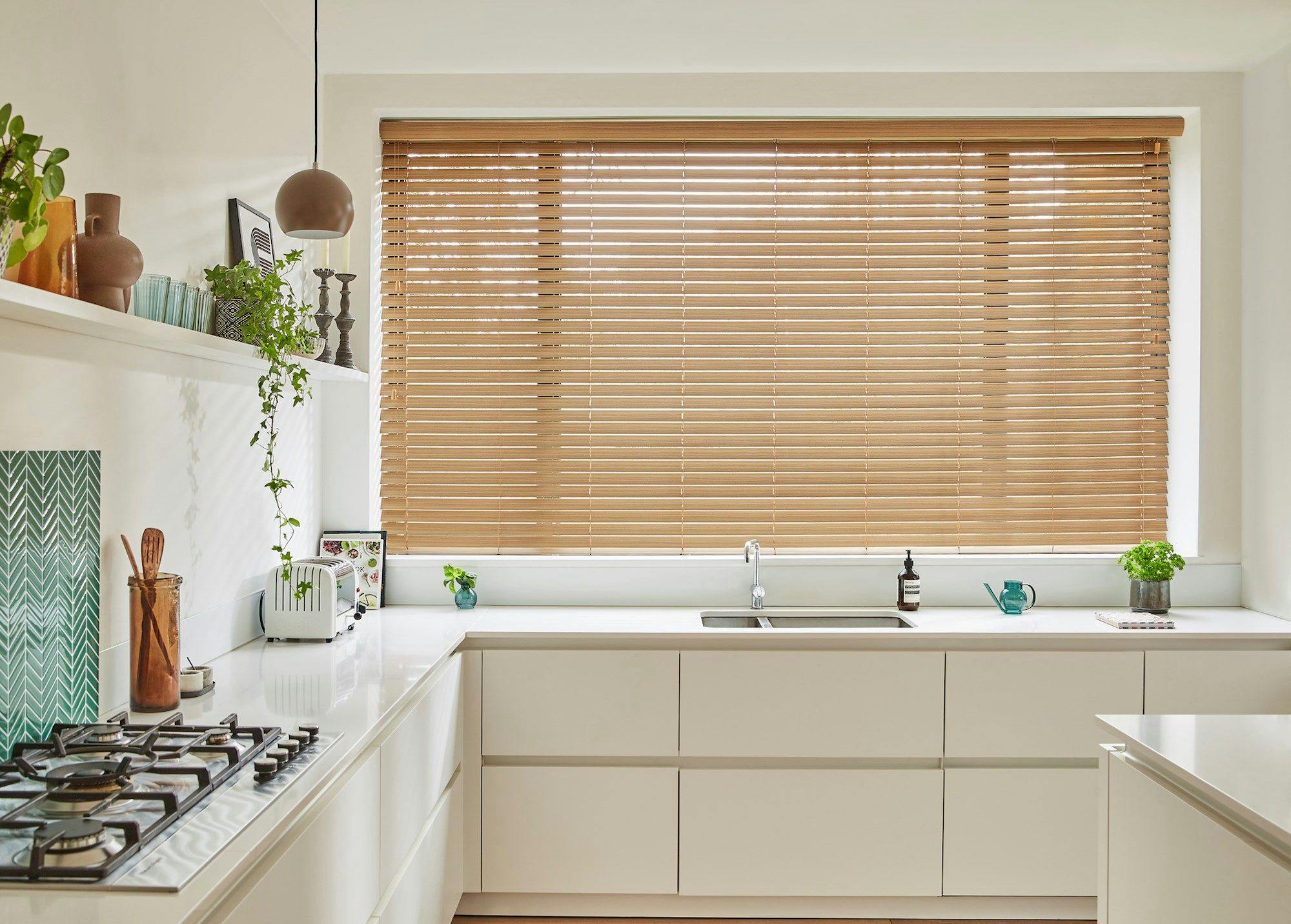 Wood Venetian Illusions blinds in a white kitchen with a sink and a cooker and hob.