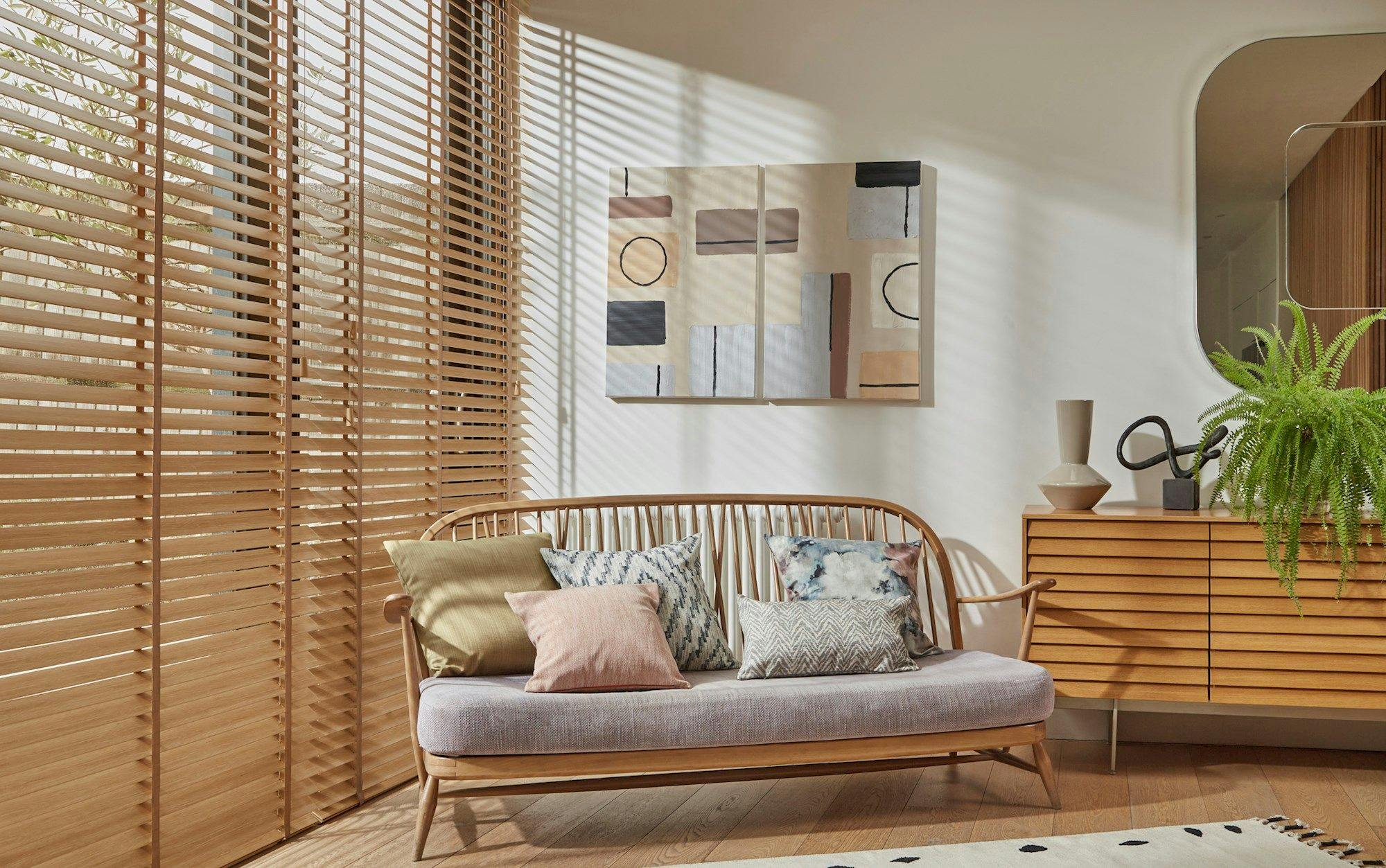 Natural Bamboo Honey blinds on the left side of the room and a wooden rattan chair in the center with art and a mirror on the wall and a wooden cabinet on the right.