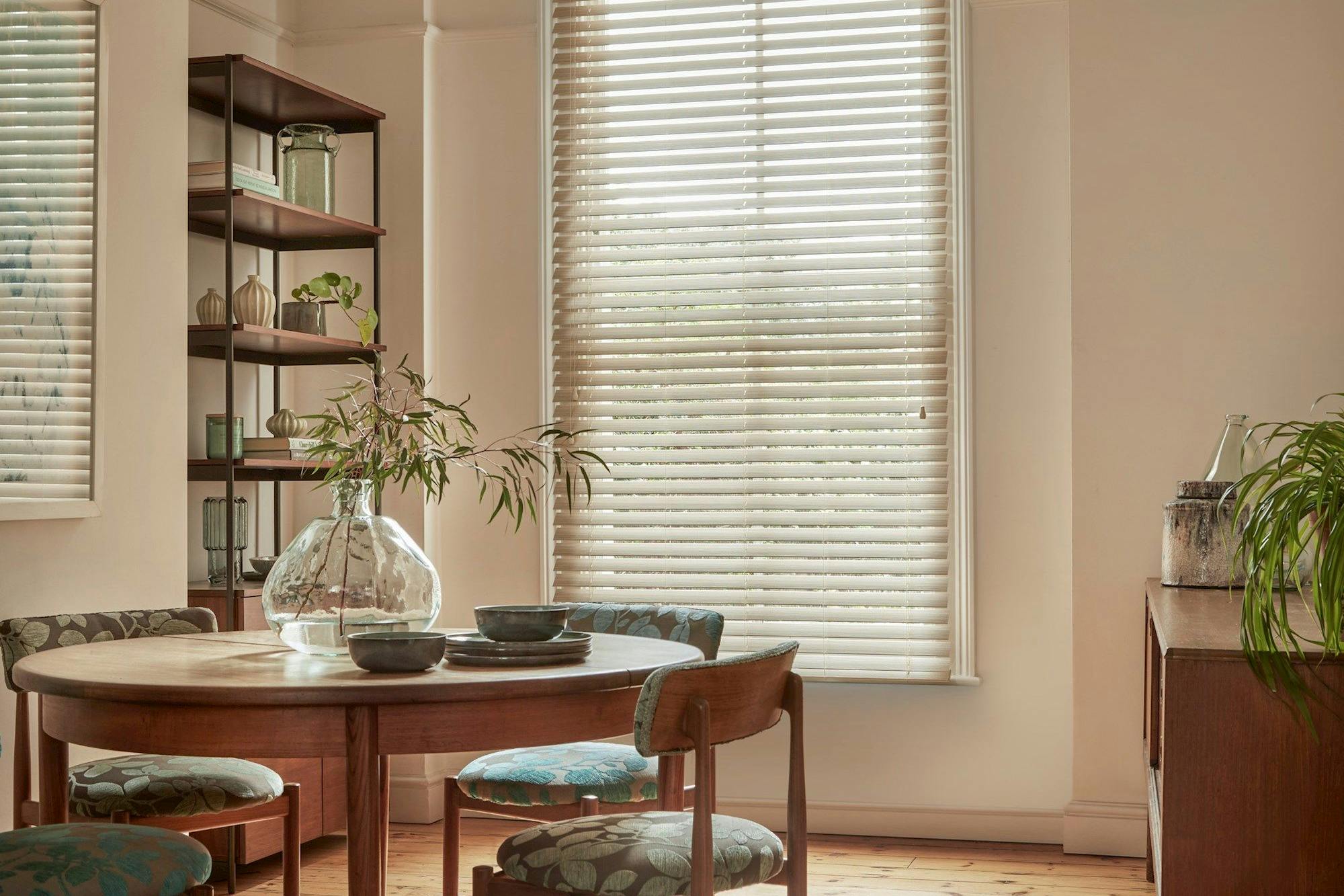 Natural Bamboo Seashell blind in a dining room with shelves on the left and a circular table with chairs to the left side and a cabinet on the right.