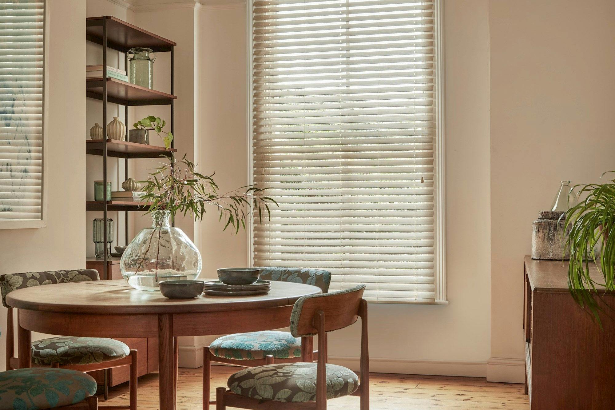 Natural Bamboo Seashell blind in a dining room with shelves on the left and a circular table with chairs to the left side and a cabinet on the right.