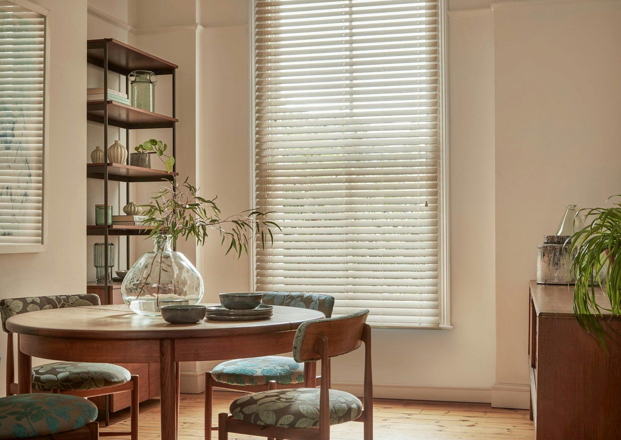 Natural Bamboo Seashell blind in a dining room with shelves on the left and a circular table with chairs to the left side and a cabinet on the right.