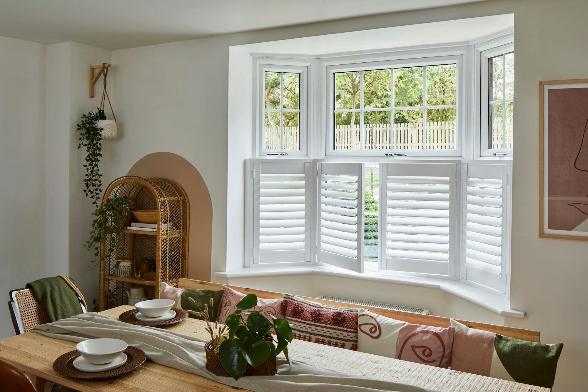 cafe style white shutters on the bottom half of a dining room window behind a furnished dining table