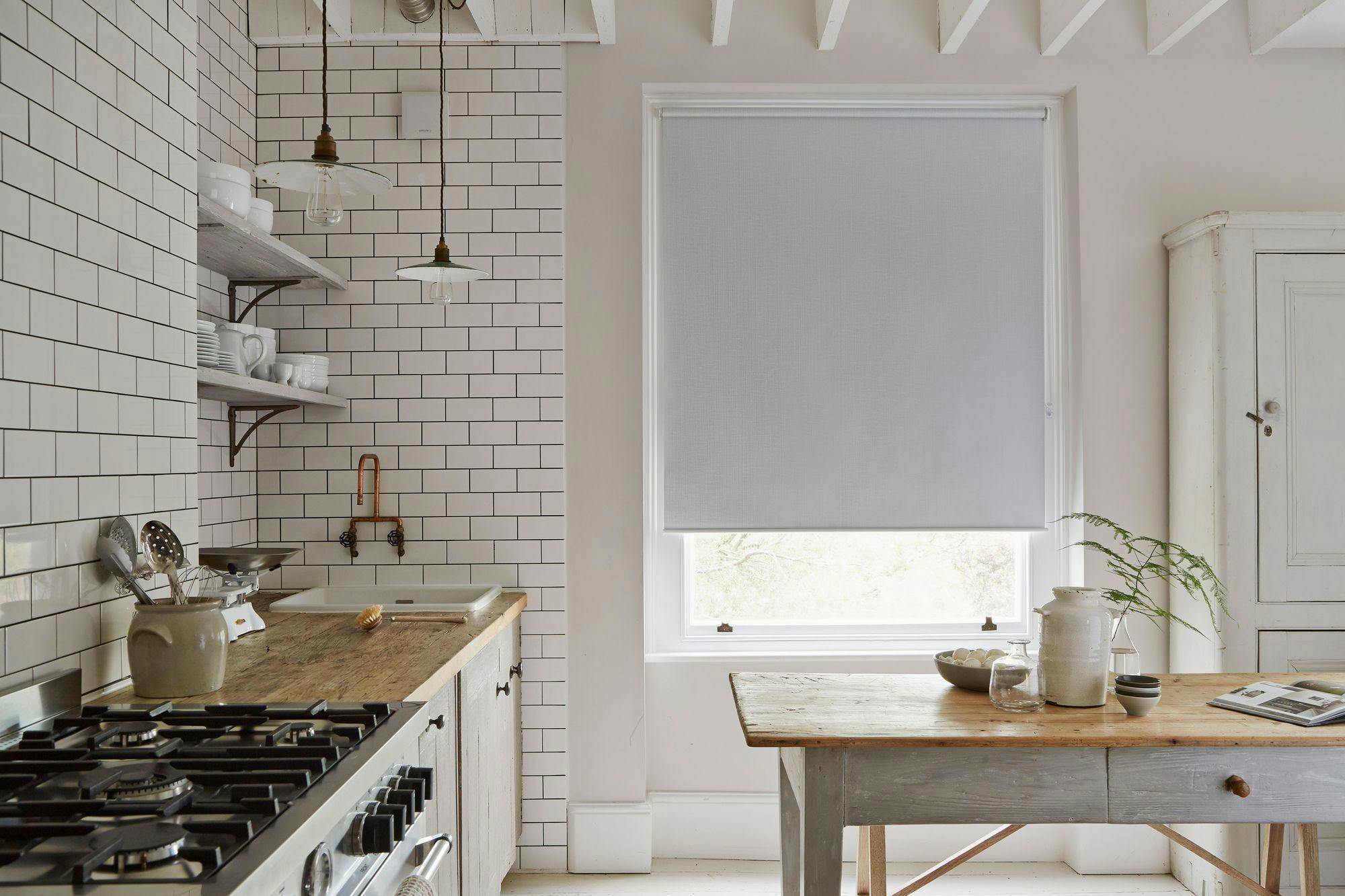 Kitchen with white subway tile walls, wooden countertops, and gas stove; a sink with utensils beside it, two pendant lights overhead, and a table with plants by a window.