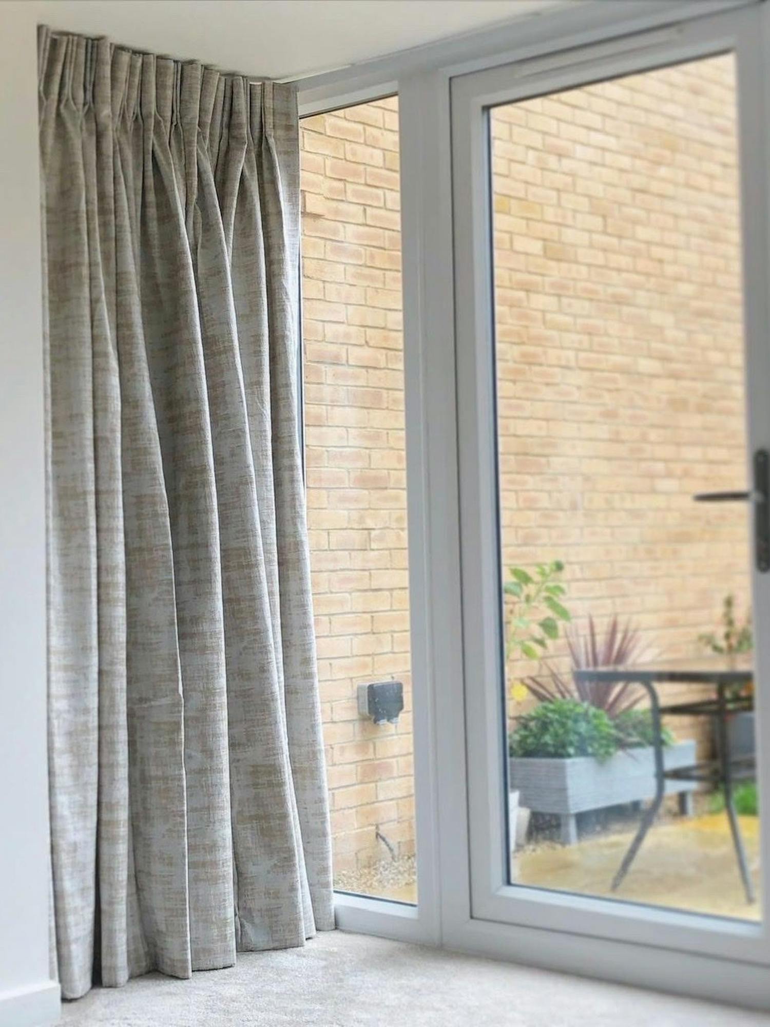 Curtains hang partially open beside a glass door, revealing an outdoor patio with a potted plant and brick wall in a bright, contemporary space.