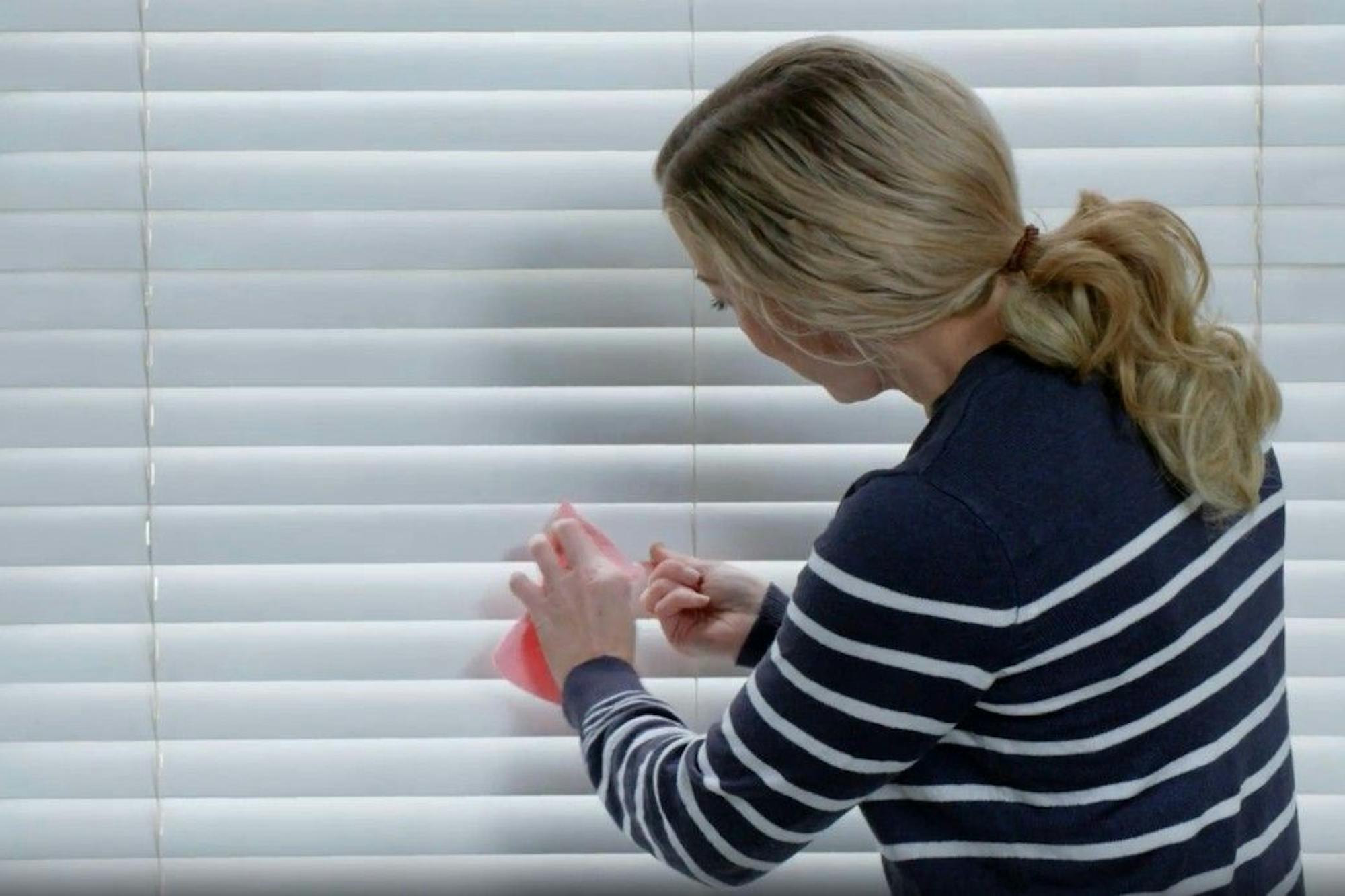woman cleaning white wooden blinds