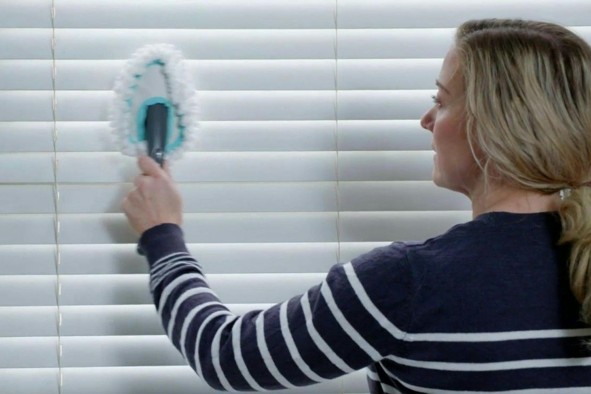 woman cleaning white wooden blinds