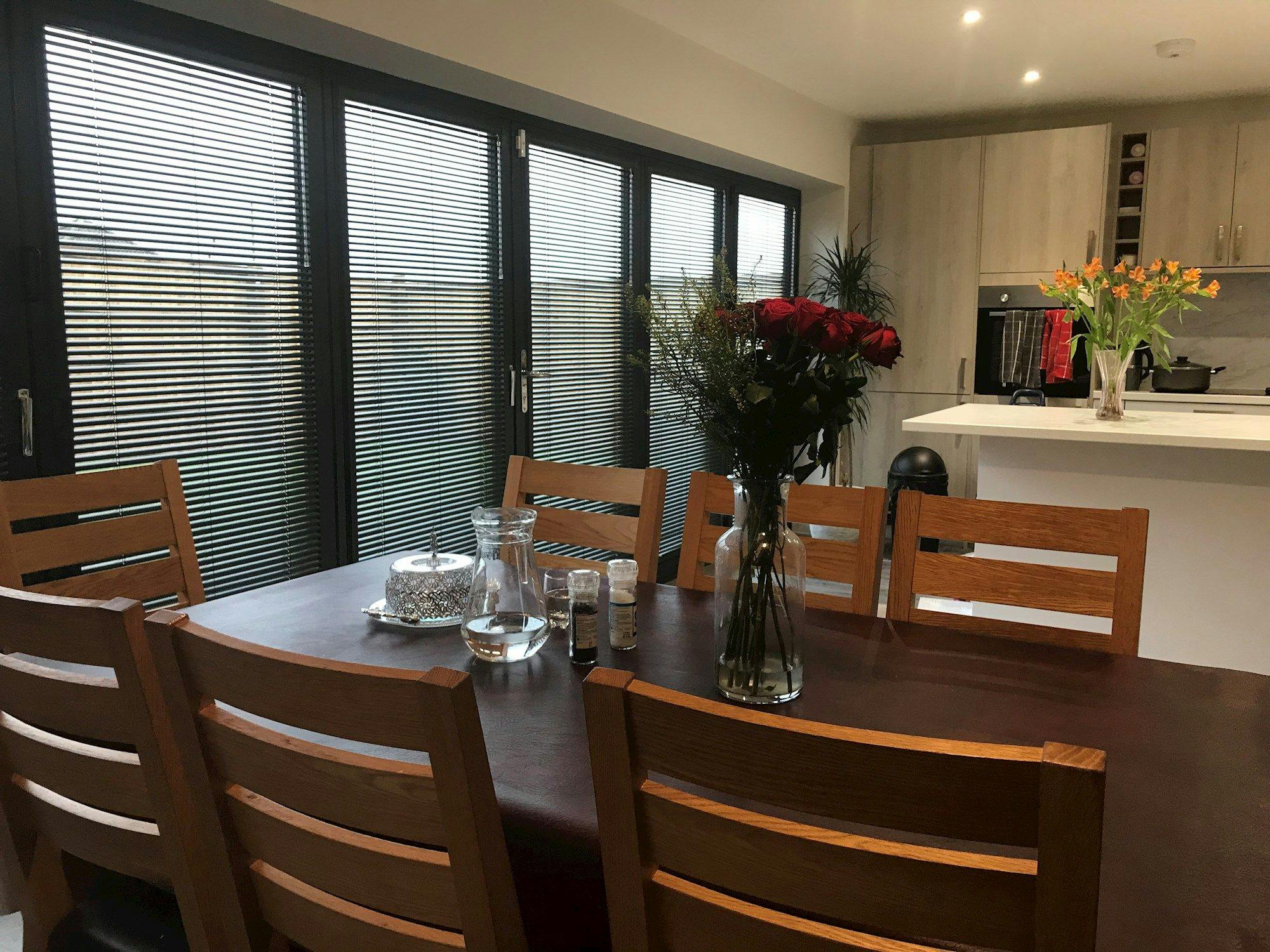 perfect fit metal venetian blinds on bifold doors in kitchen with dark brown dining table