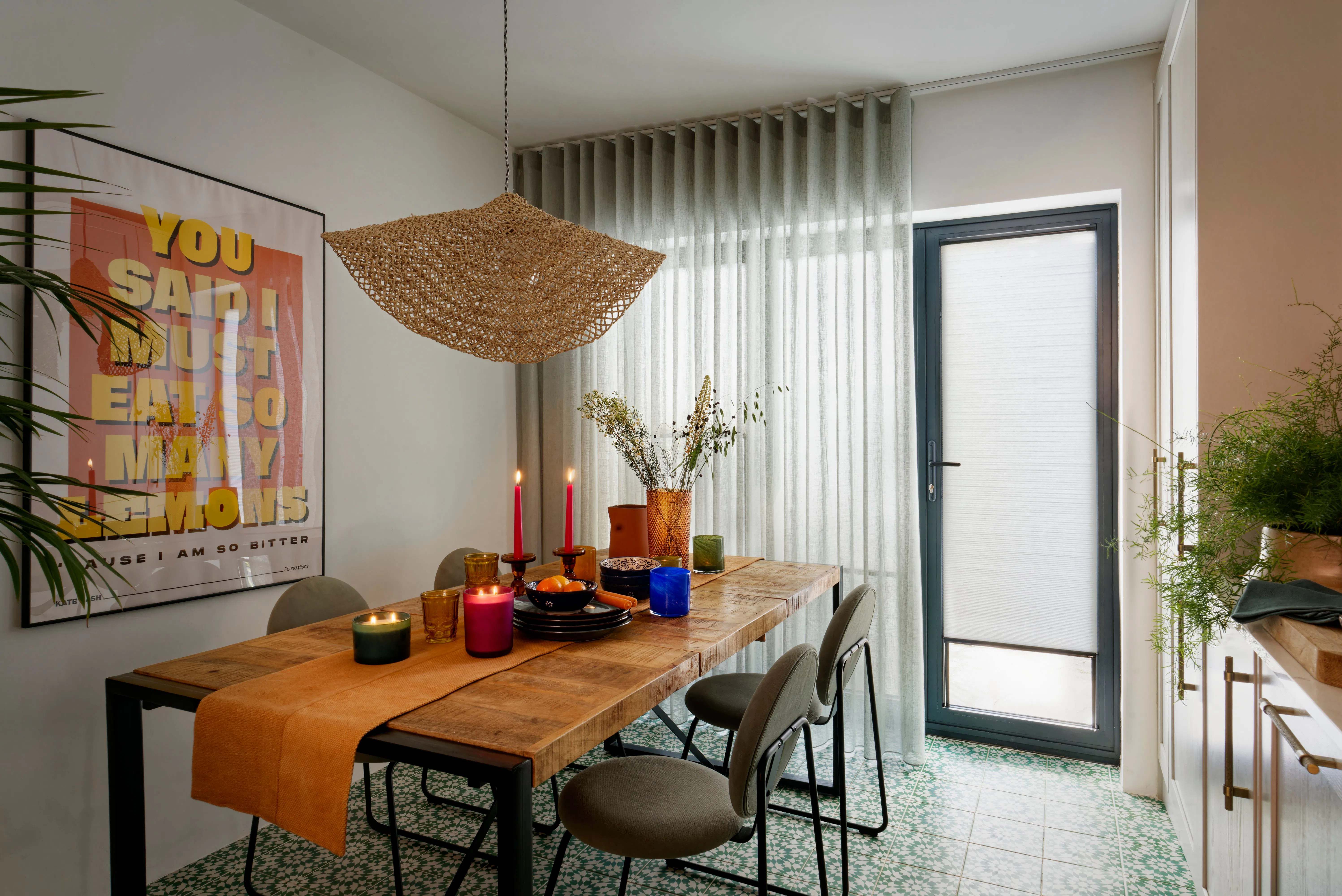 Dining table with candles and dishes, set in a room with sheer curtains and wooden decor. A wall poster reads, "YOU SAID I MUST EAT SO MANY LEMONS CAUSE I AM SO BITTER."