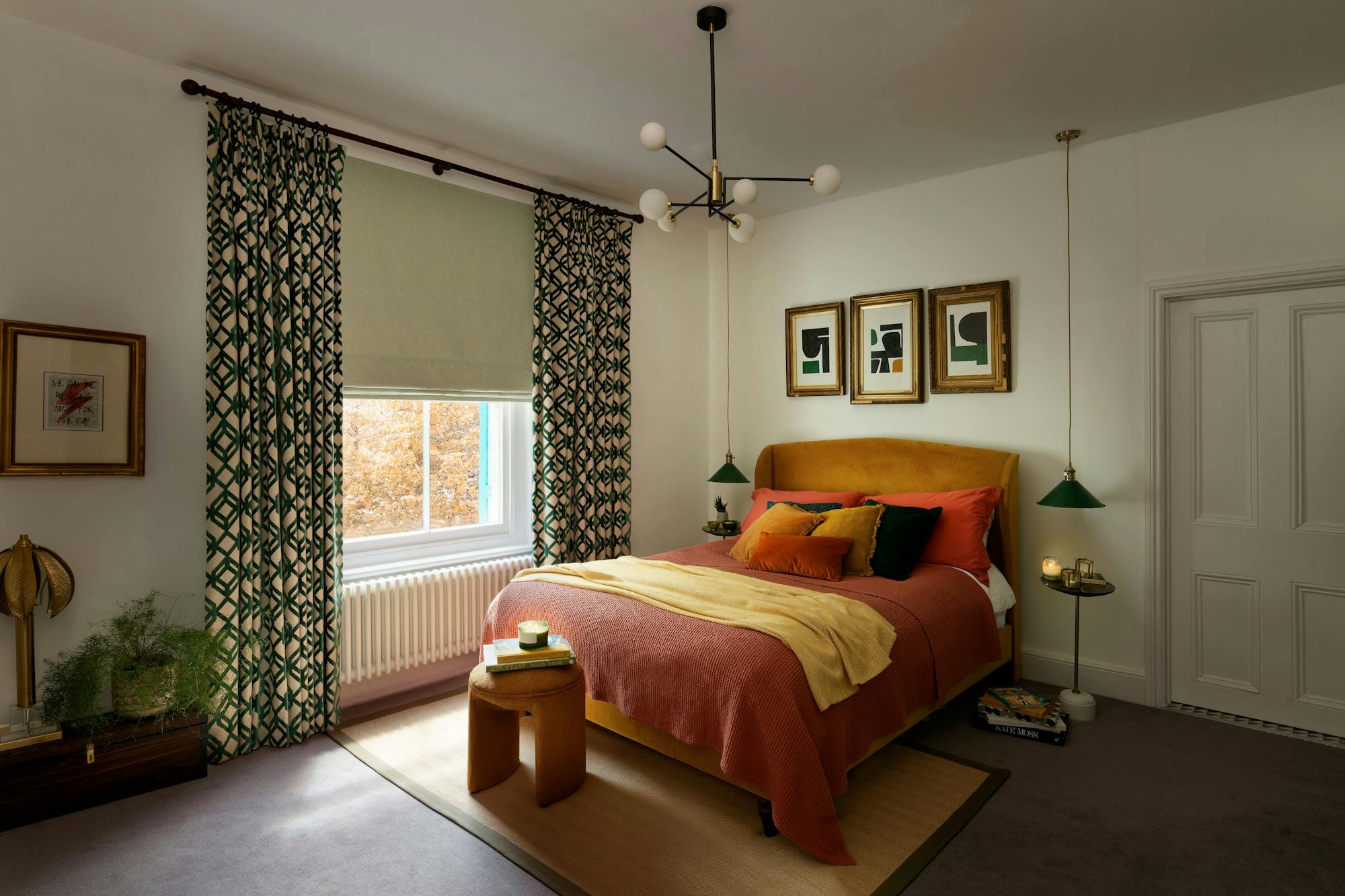 A comfortable bedroom features a bed with colorful pillows and a throw blanket, accompanied by modern lamps and artwork. The room is illuminated by a window with patterned curtains.
