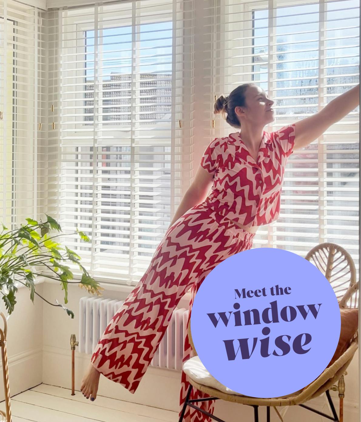 Woman in a red zigzag outfit adjusts white blinds in a bright room with large windows, a chair, and a plant. Text reads, "Meet the window wise."