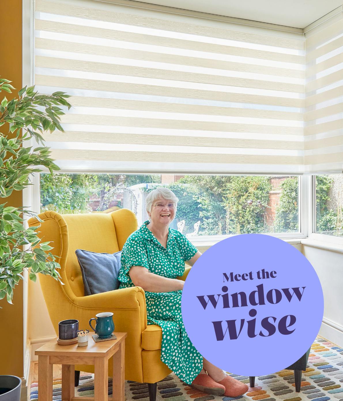 A person sits smiling in a yellow chair by large windows with striped blinds. A plant and two mugs are nearby. Text reads, "Meet the window wise."