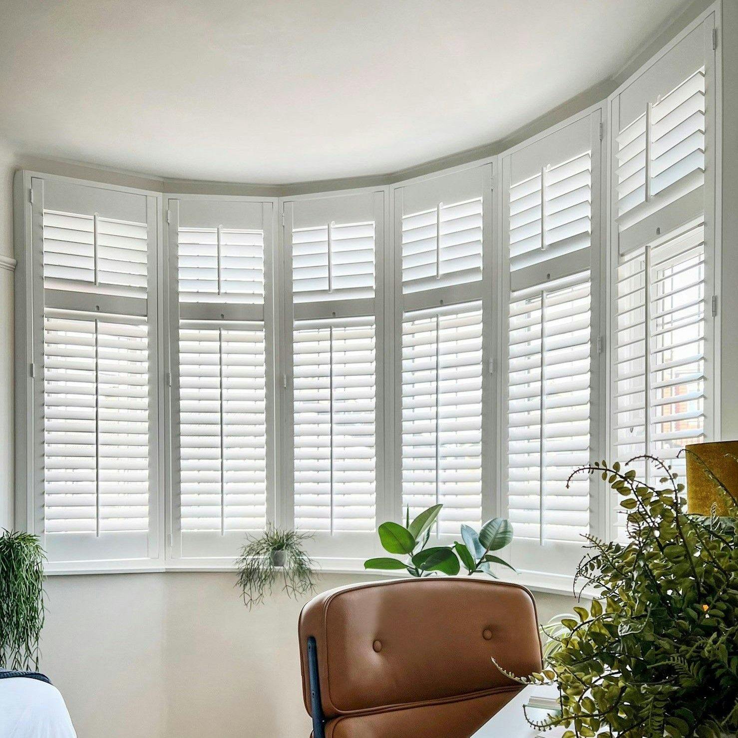 pure white shutters on a curved bay bedroom window with a copper lightshade and cosy furnishings