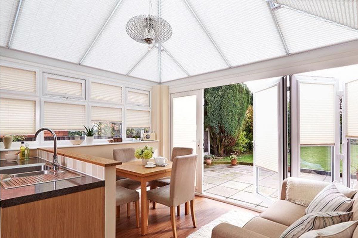 Conservatory dining room with bi-fold doors and montoya sand pleated roof blinds