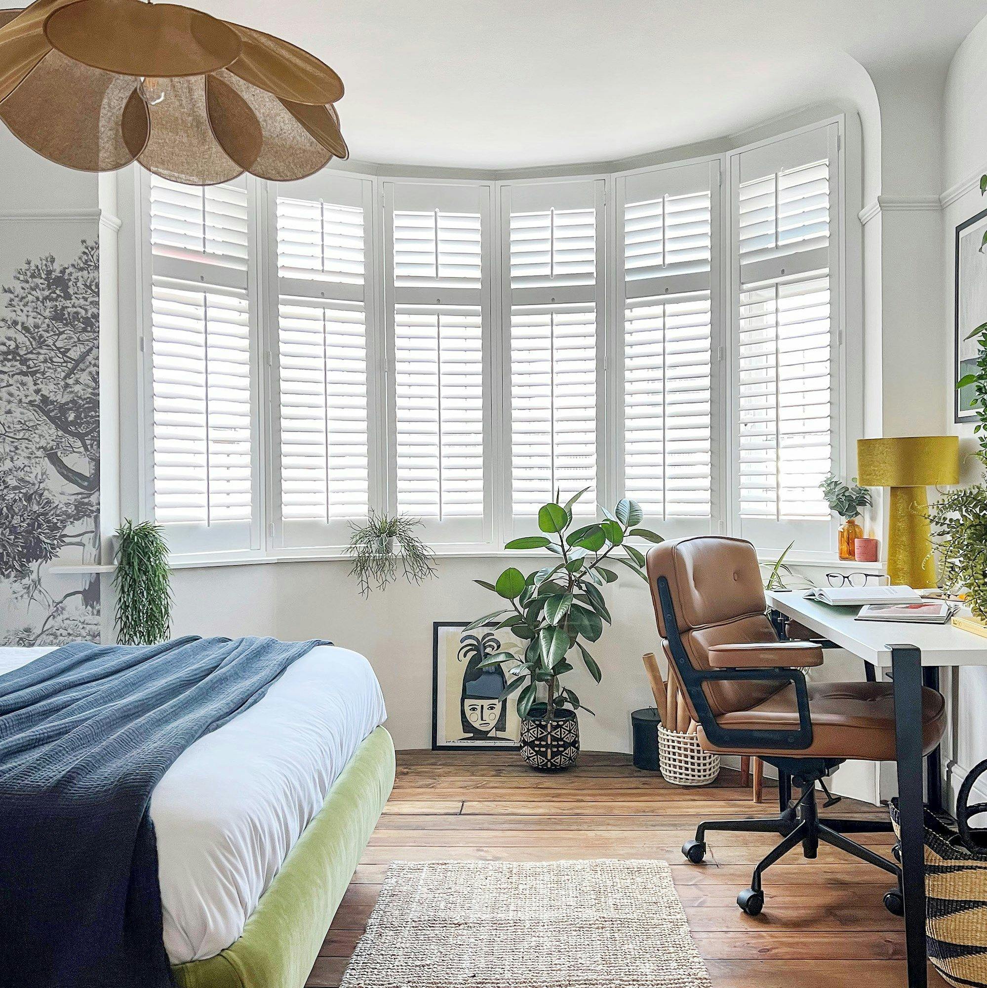 pure white shutters on a curved bay bedroom window with a copper lightshade and cosy furnishings