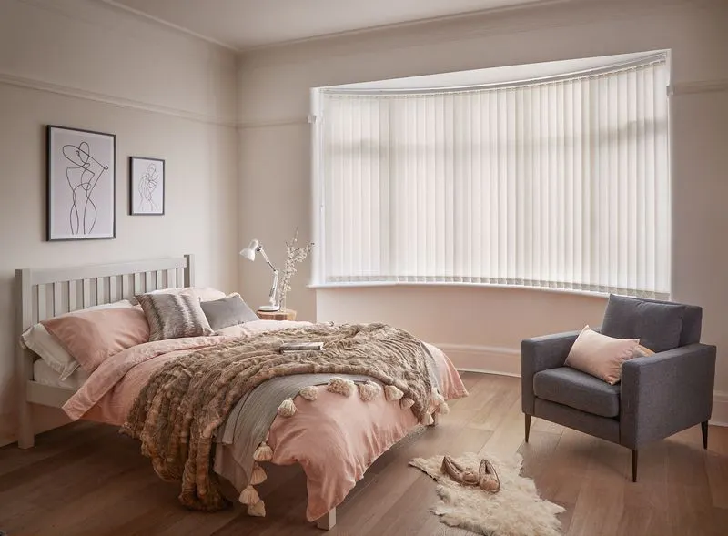 Minimal luxe bedroom with soft furnishings and a bow window dressed with light cream vertical blinds 