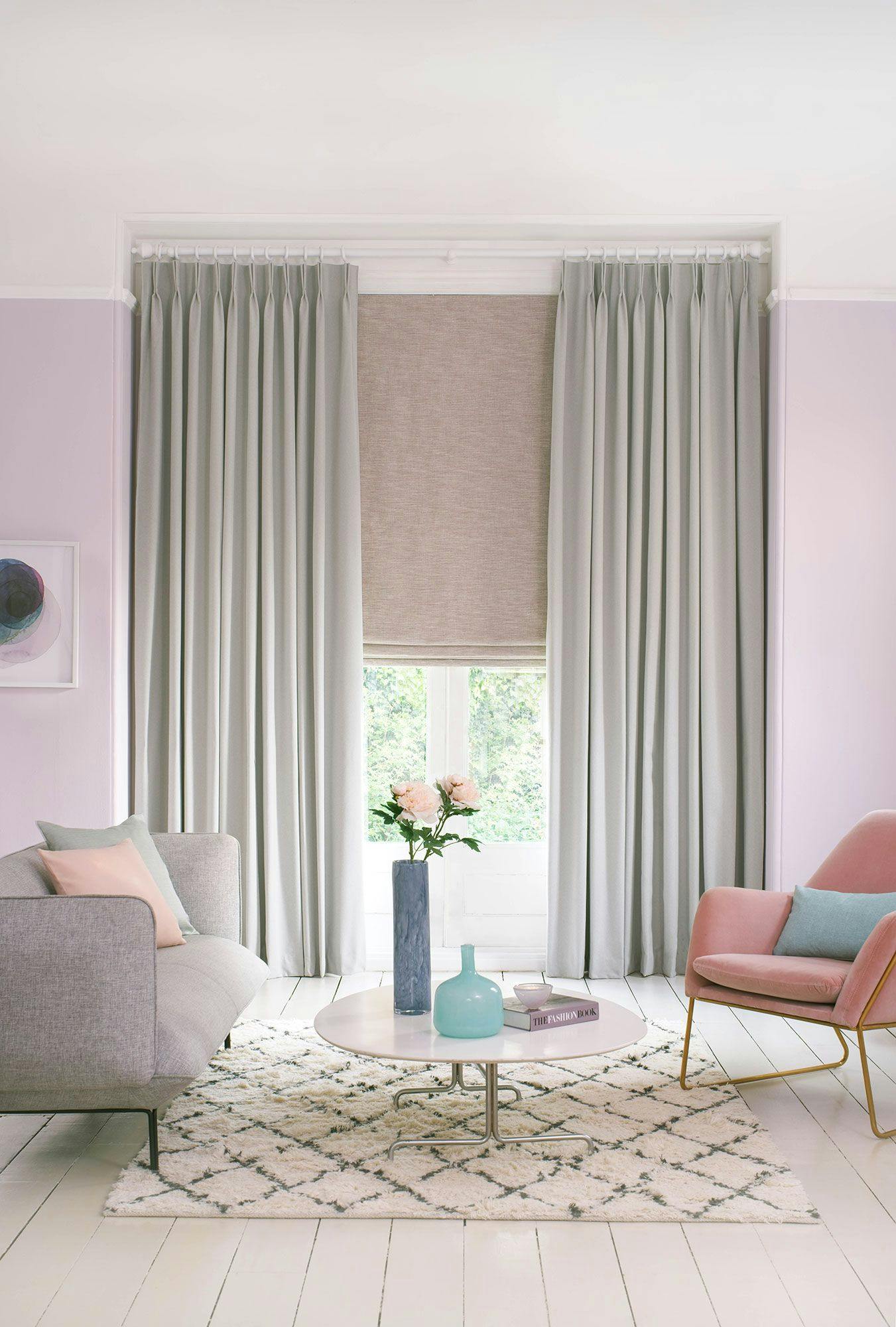 Huxley Dove Grey curtains with a Haddie Chalk Pink roman blind in soft pink living room. Two chairs are featured in this image along with a table that has vases and a book