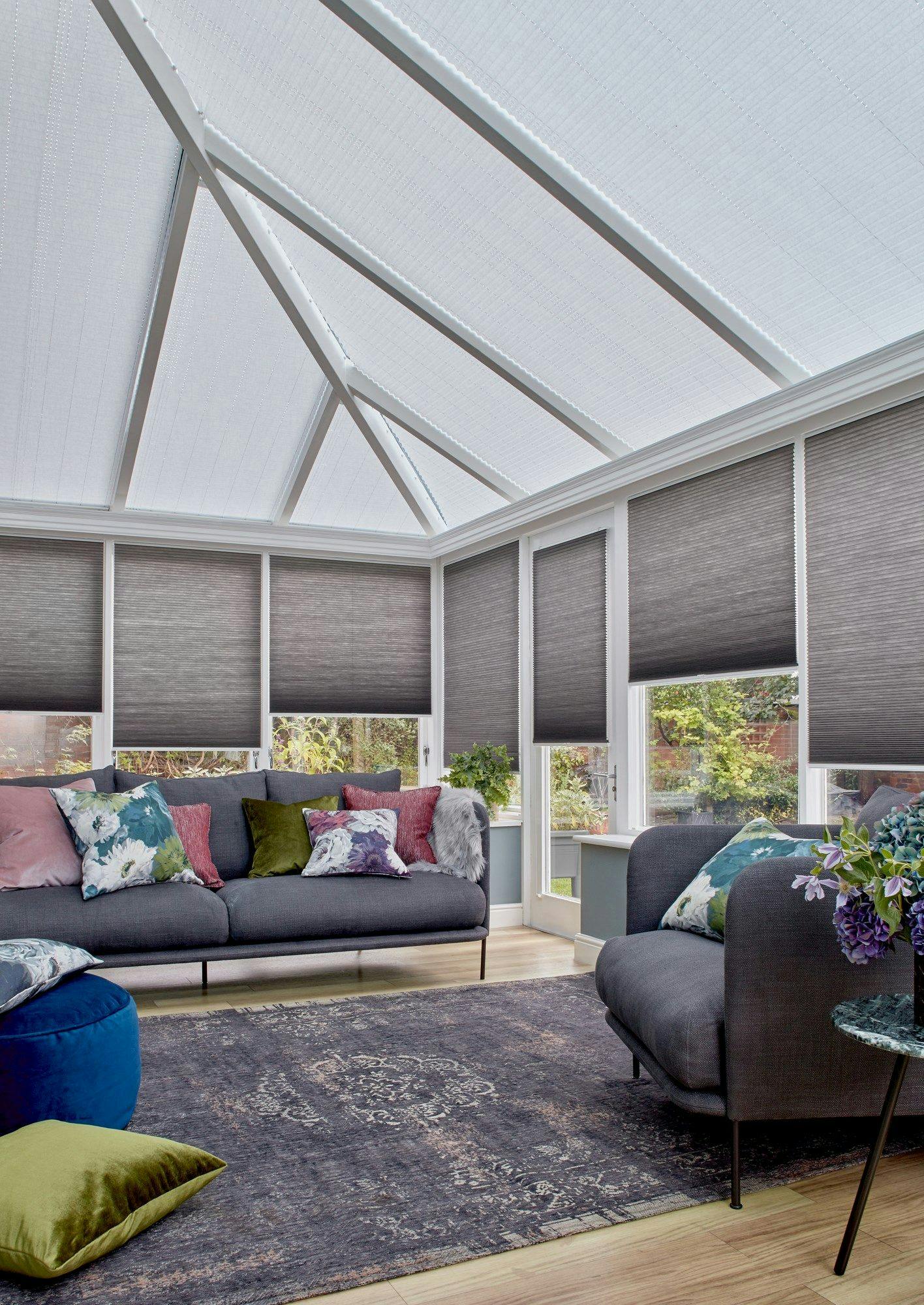 Charcoal Thermashade Pleated blinds at varying drop heights dressed on the windows in conservatory. Grey sofa with cushions and a large grey rug are also in situ.