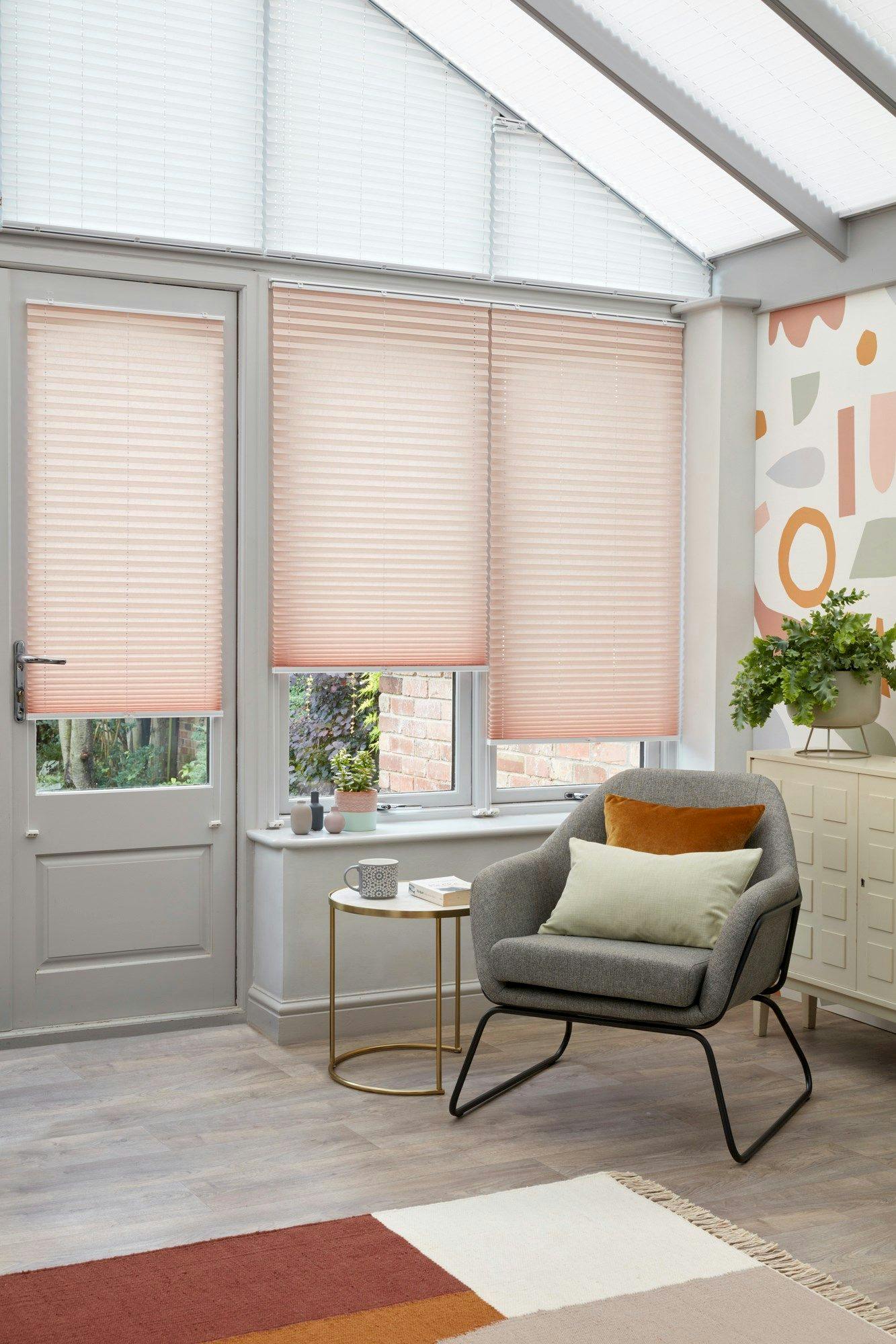 Peachy pink Pleated blinds hanging at varying drop heights on the conservatory doors and windows and upper windows are dressed with white Highgrove pleated blinds.