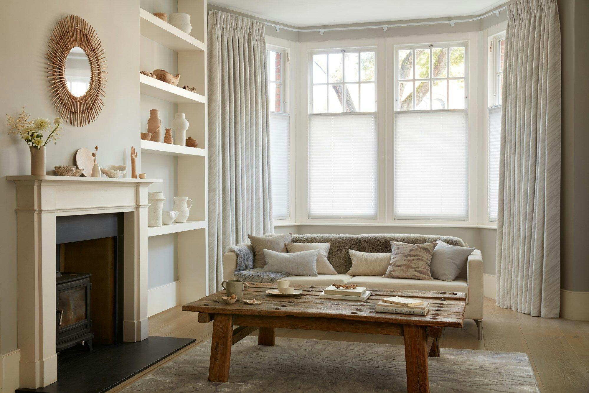 White curtains featuring light grey pattern on curtains dressed over cafe style Pleated blinds on windows of living room.