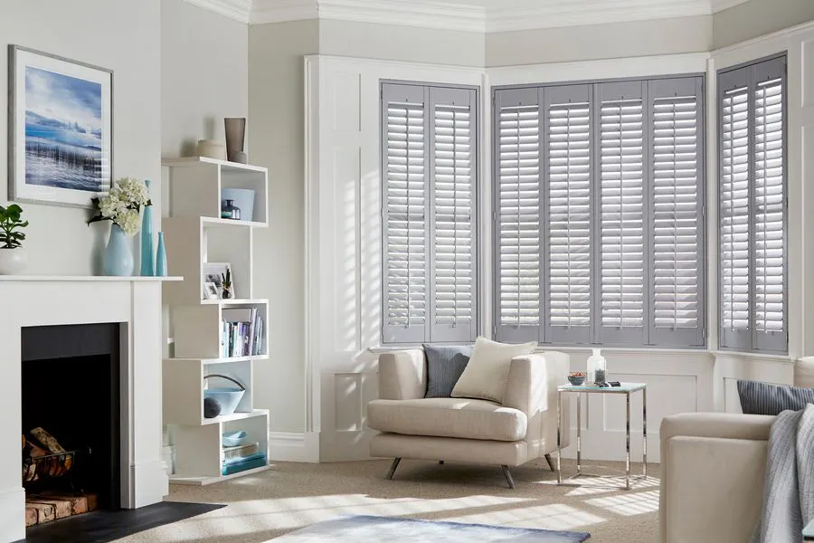Grey tracked shutters fitted to a bay window in a living room